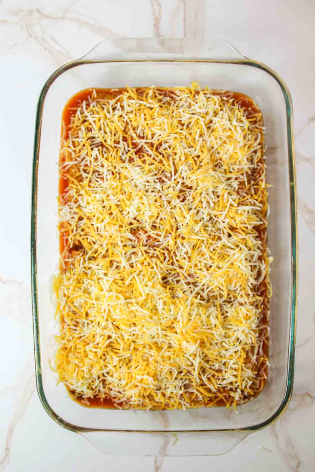 taquitos covered in enchilada sauce and shredded cheese in 9x13 baking dish