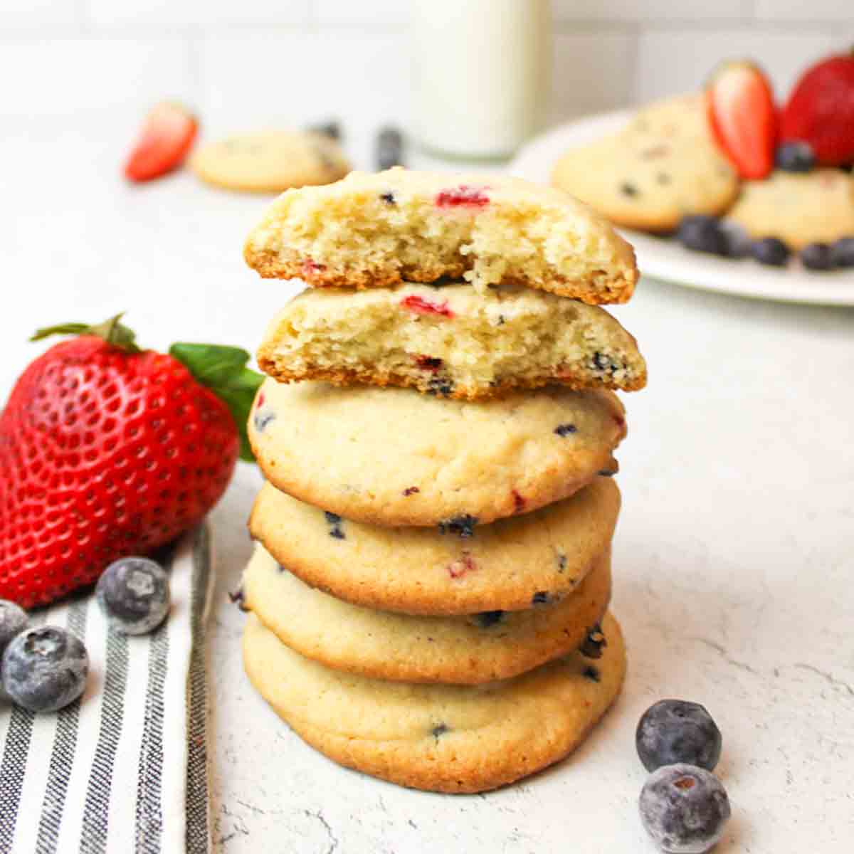 stacked muffin mix cookies with top cookie broken and fresh berries scattered around.