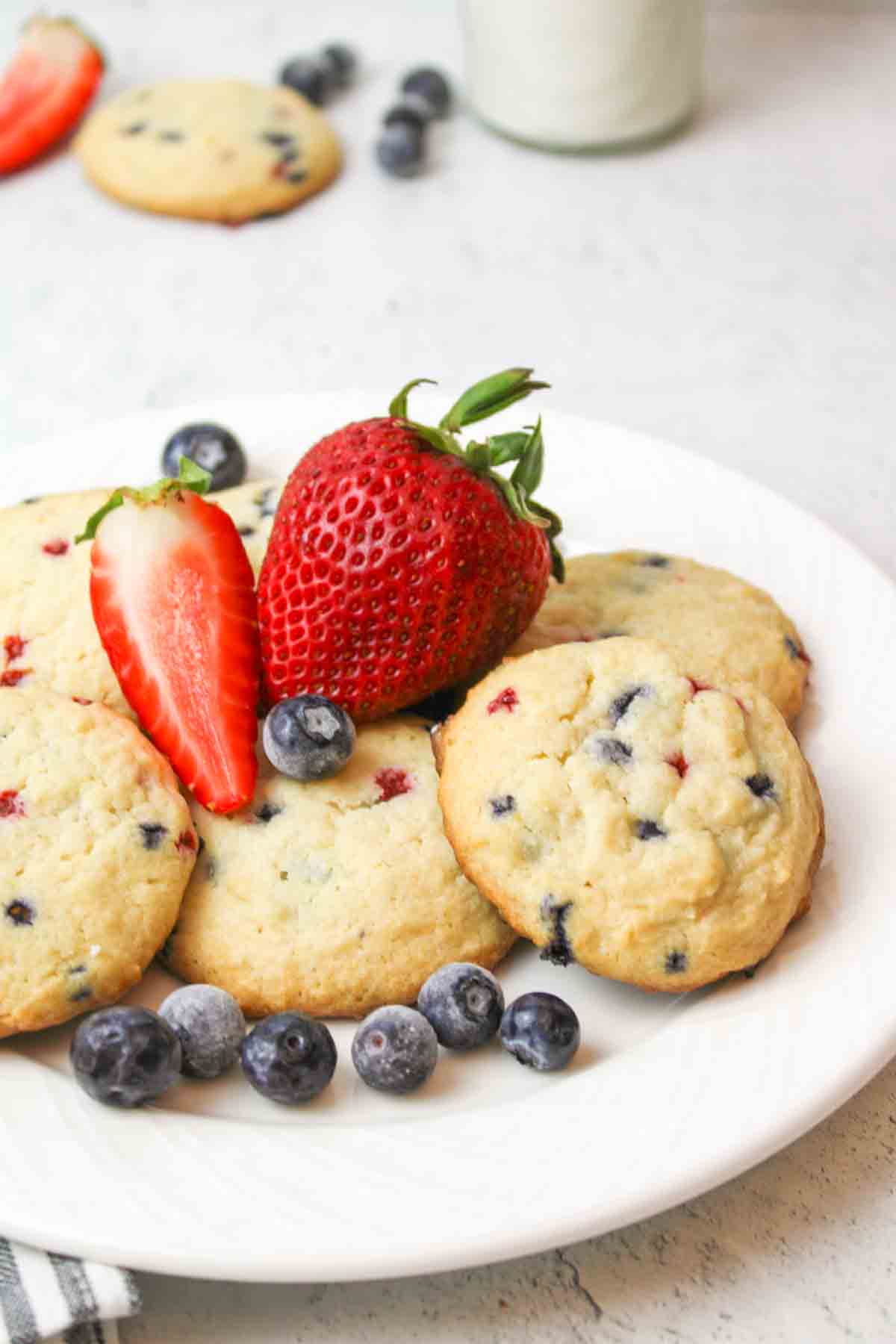 White plate with triple berry muffin mix cookies, topped with blueberries, strawberries.