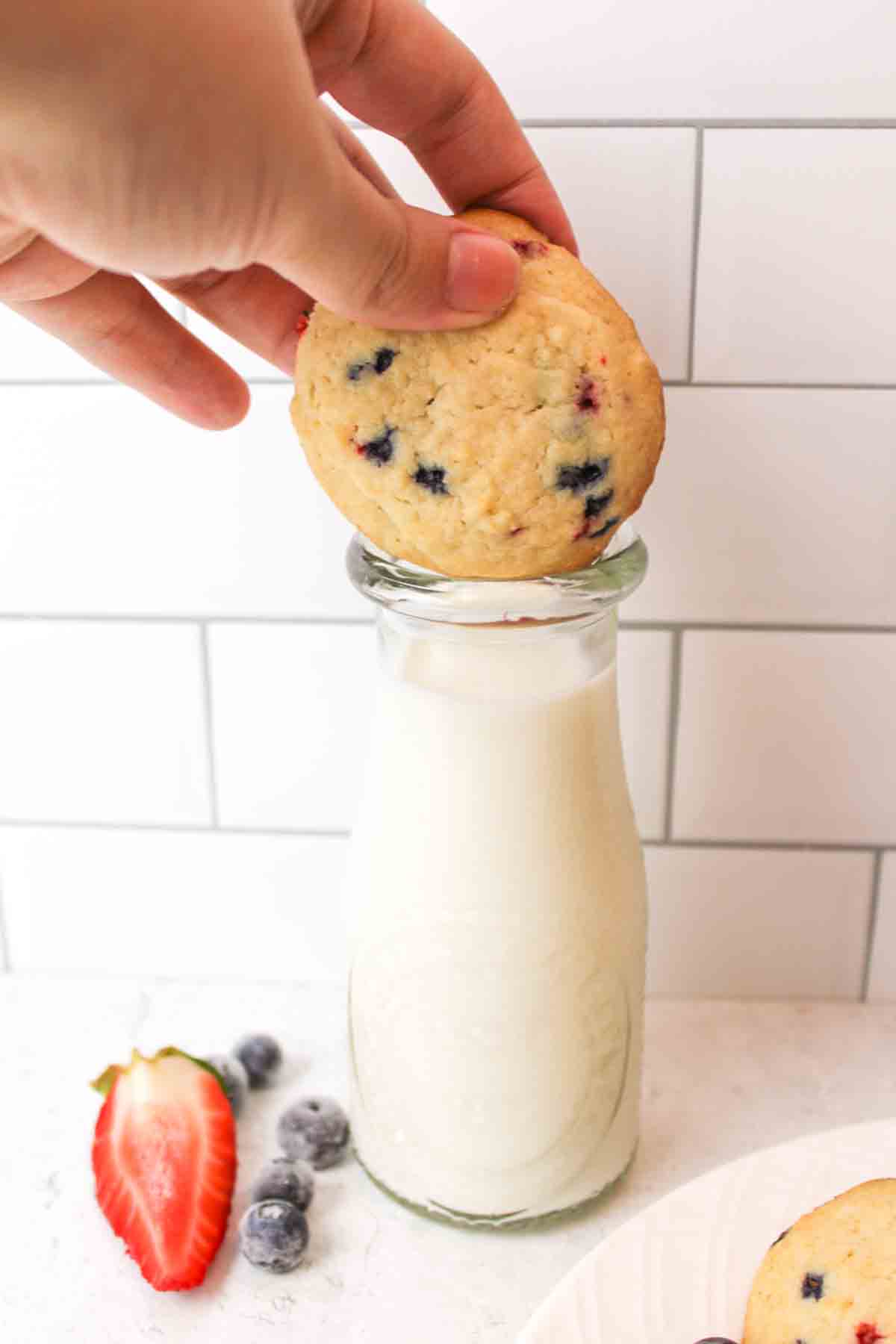 a hand trying to dunk a muffin mix cookie into a bottle of milk