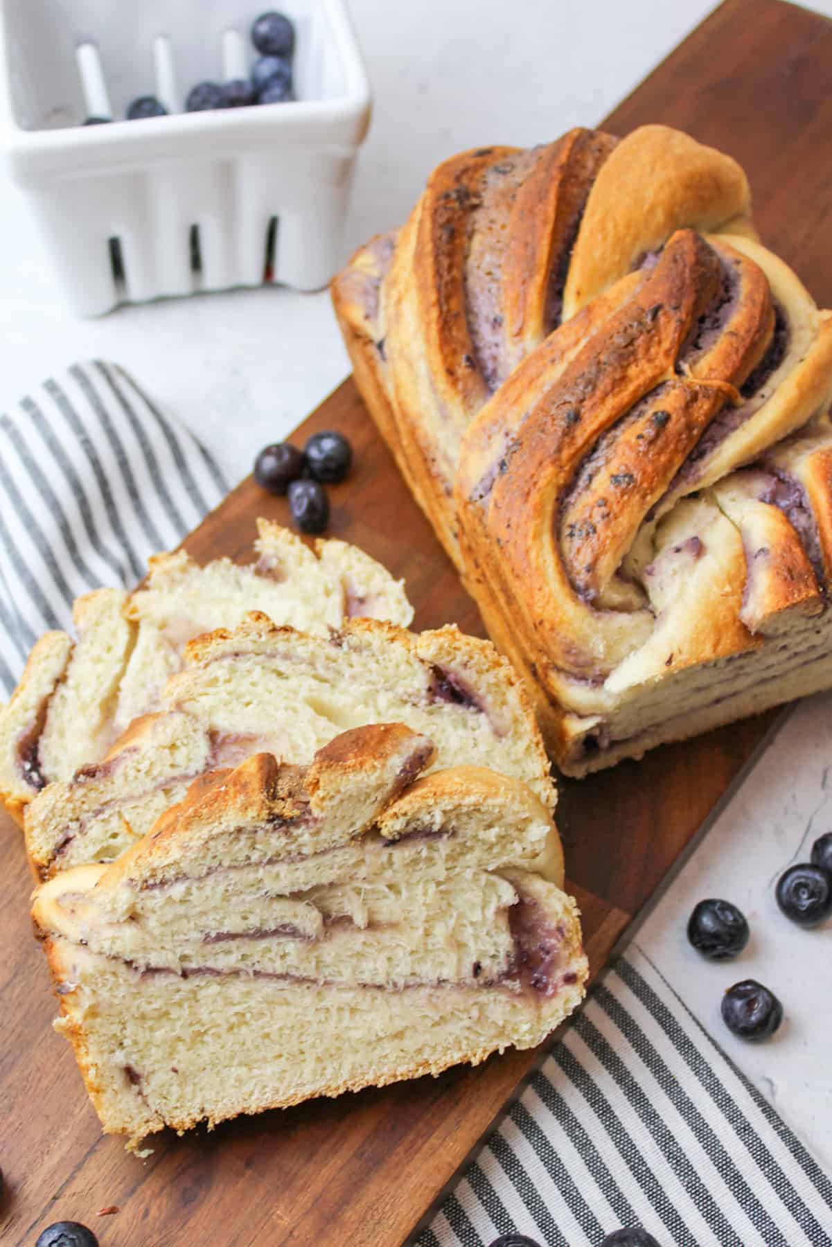 sliced Blueberry Cream Cheese Babka on a wooden boad with fresh blueberries scattered around