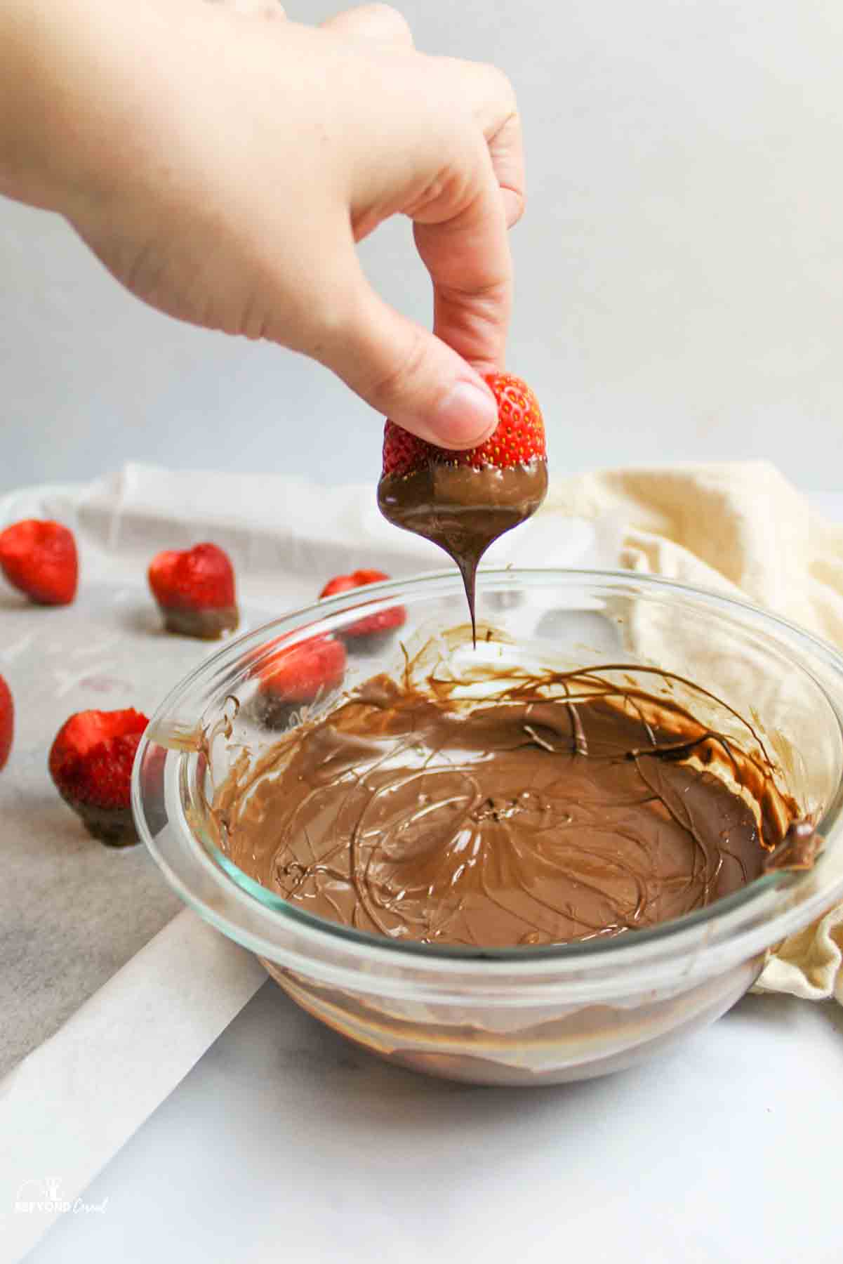 dipping strawberries into melted chocolate and holding it above chocolate to drizzle off the excess.