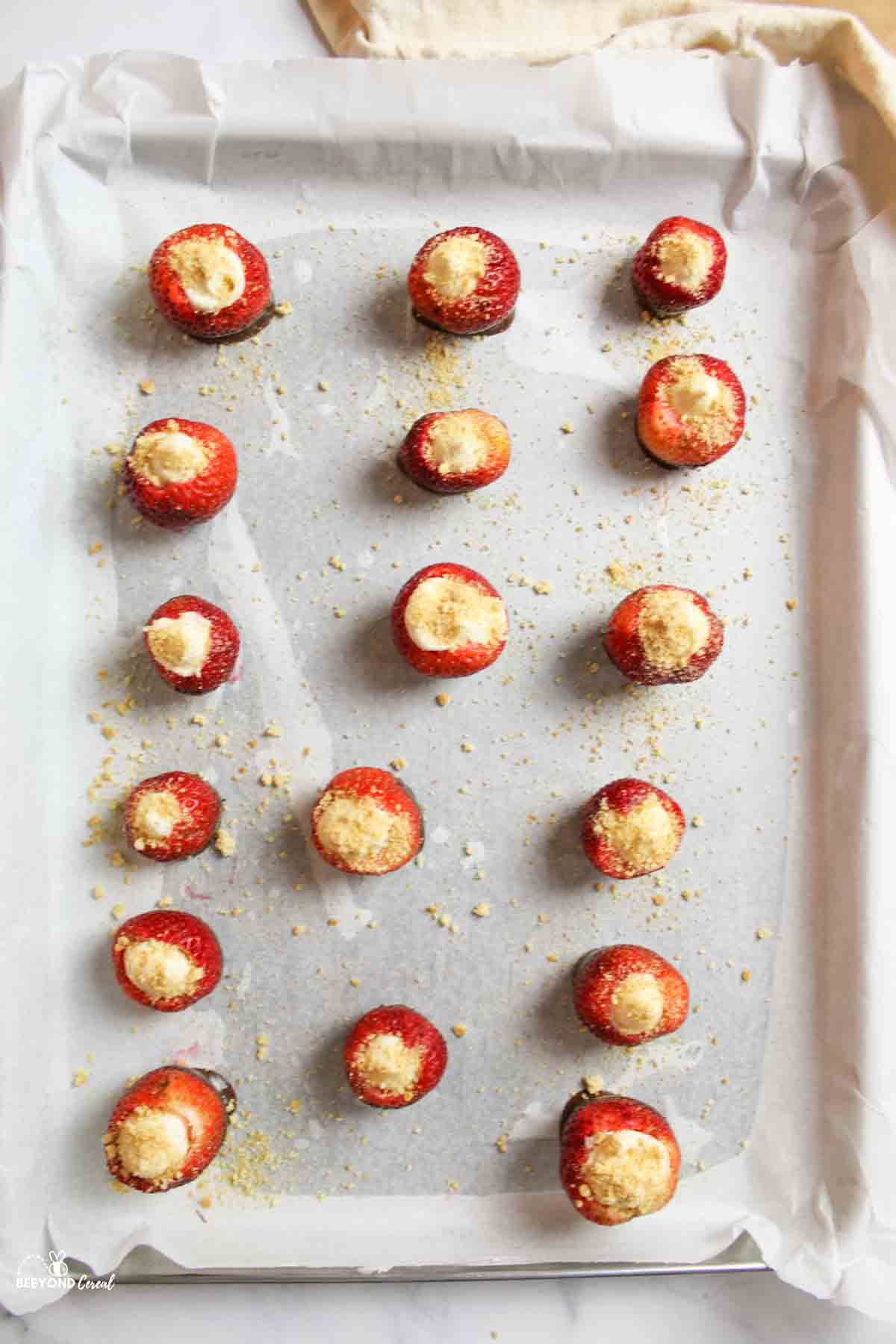 graham cracker crumb topped cheesecake stuffed strawberries on parchment paper lined baking sheet.