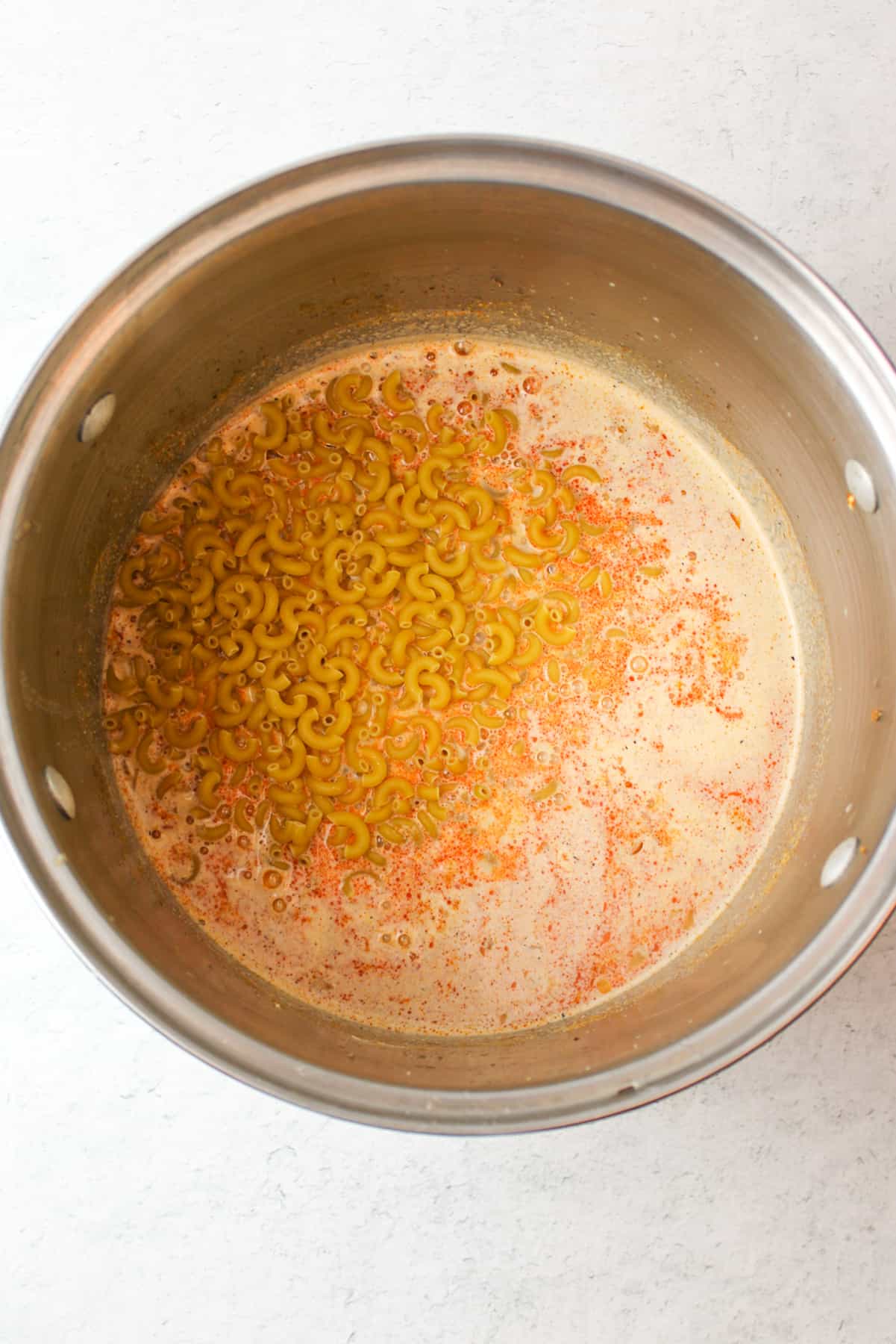 dry elbow noodles added to a large pot of orange liquid
