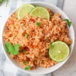 salsa rice in a white bowl with lime wedges and cilantro.