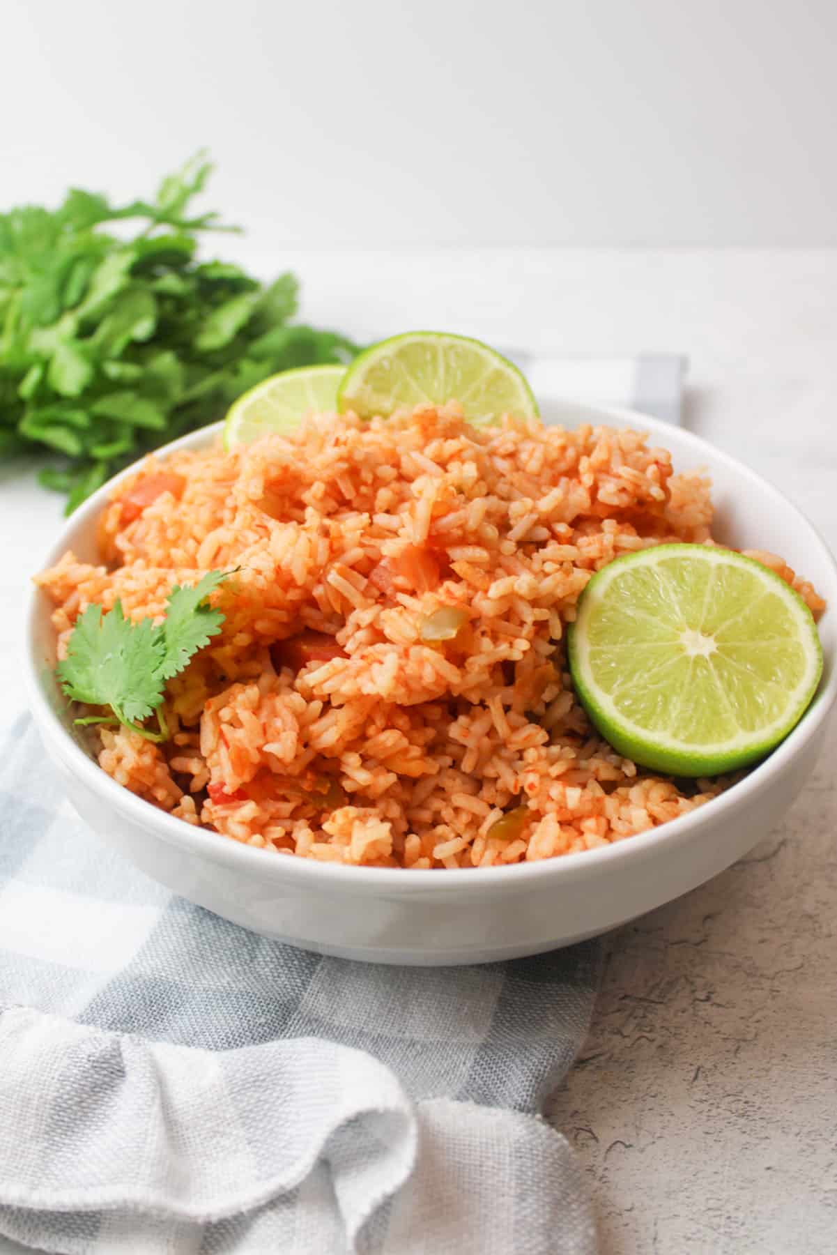 a white bowl filled with salsa rice and garnished with sliced limes and cilantro.