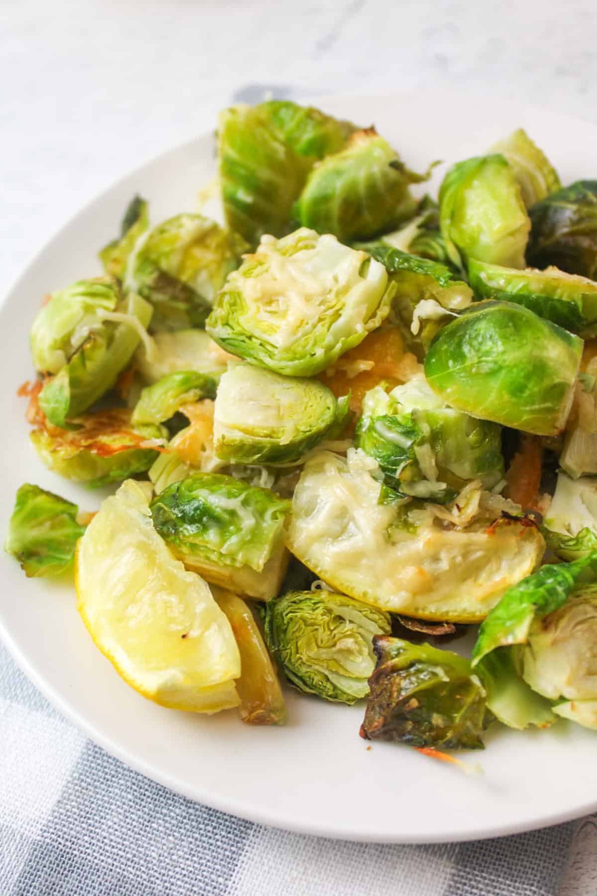 roasted garlic brussel sprouts with parmesan cheese and lemon wedge on a white plate