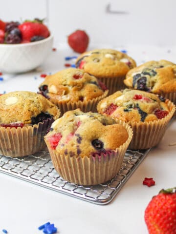 red white and blue muffins on a wire cooling rack with fresh fruits and patriotic sprinkles around them