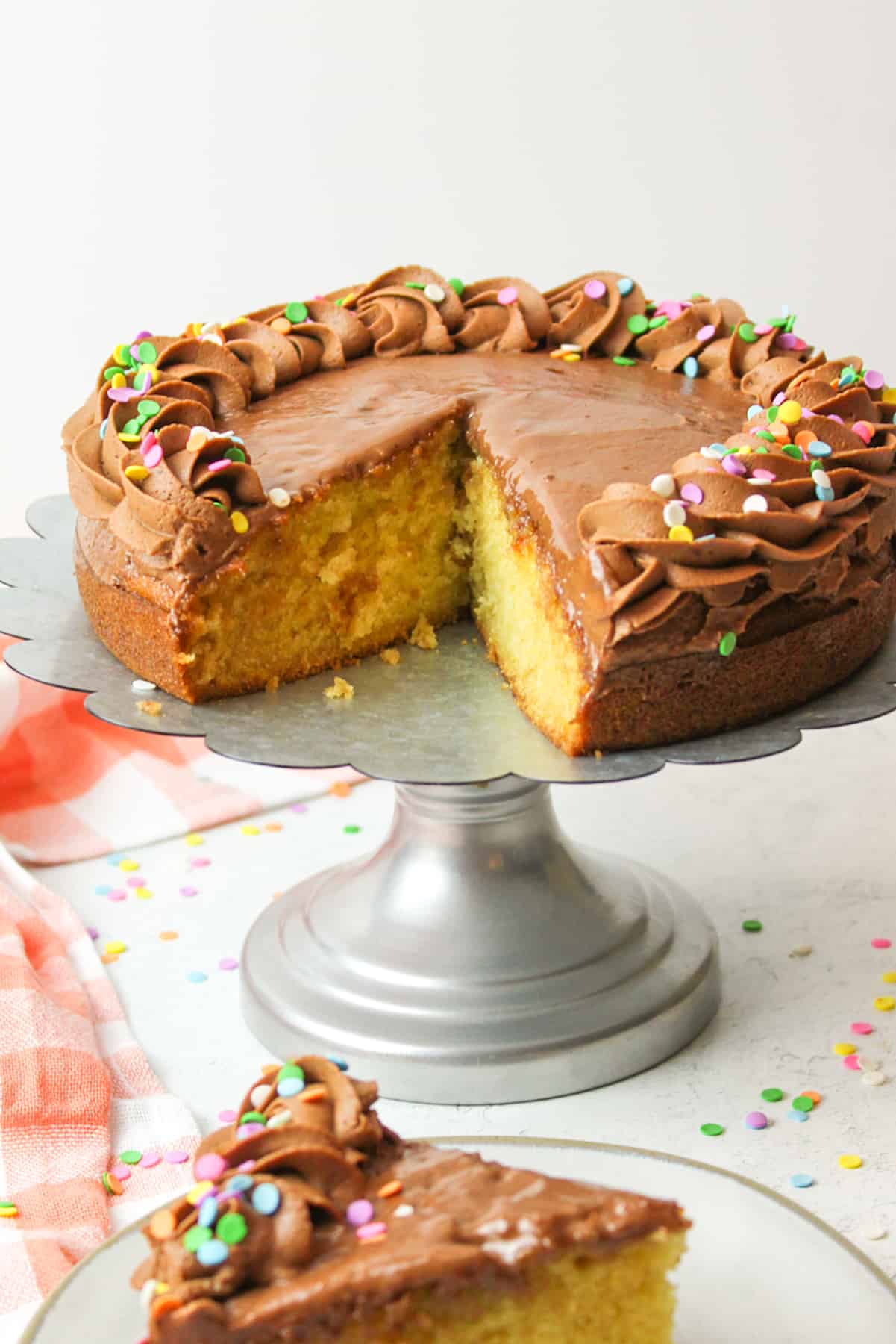 a sliced yellow cake with chocolate frosting on a metal cake stand.