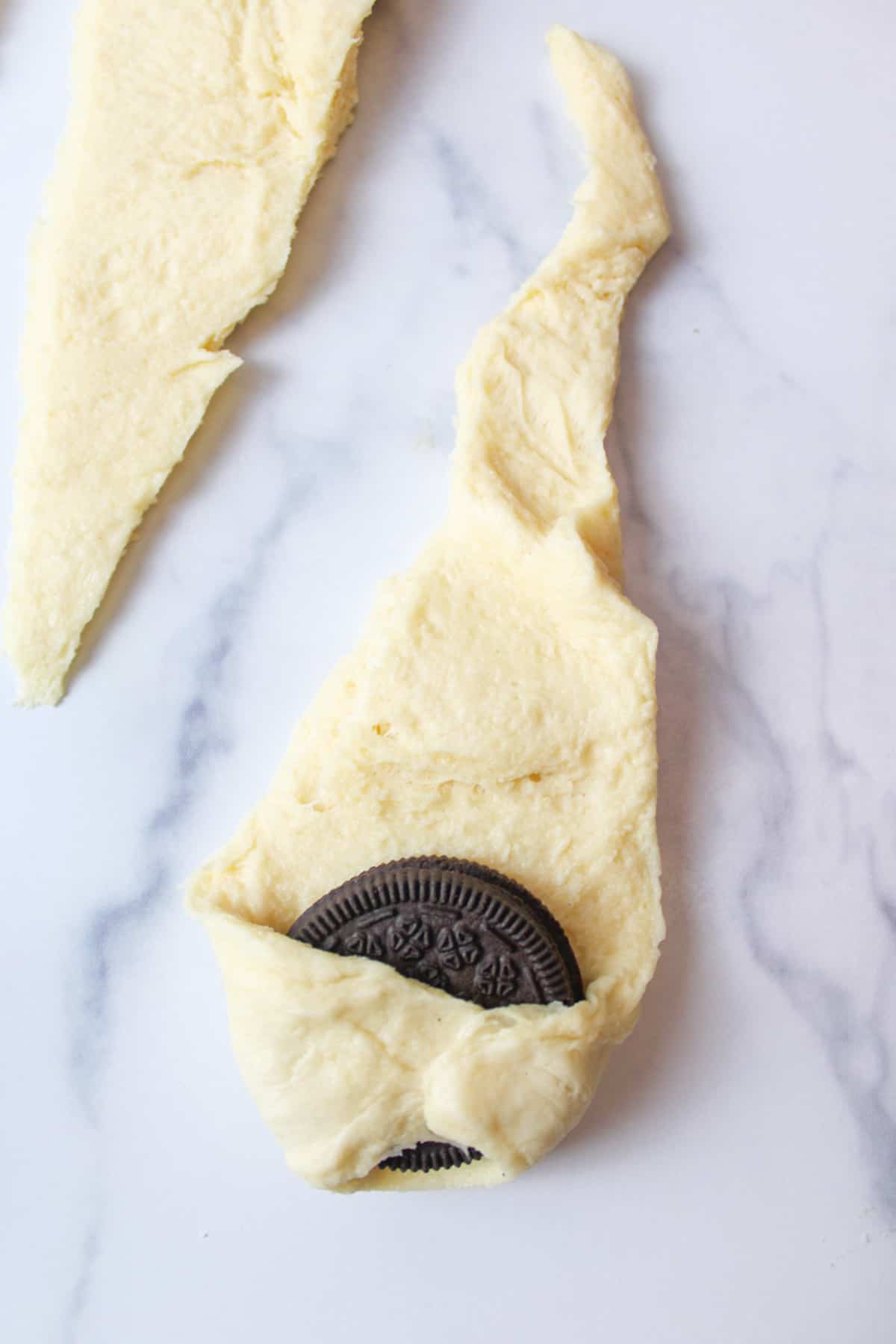 upclose view of the corners of triangle shaped crescent roll dough curled up over the oreo cookies
