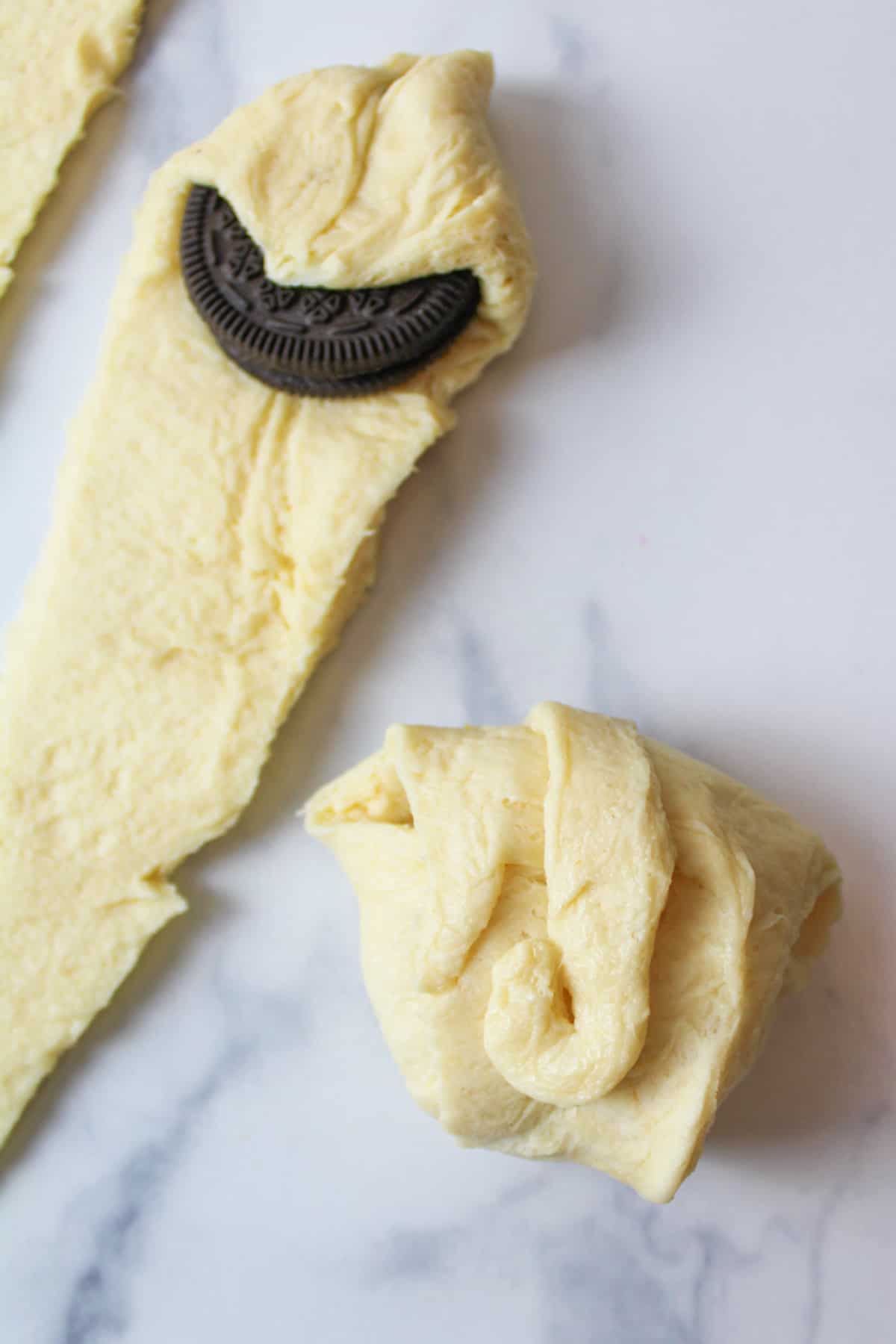 an oreo cookie partially covered in dough with one oreo cookie covered completely in crescent roll dough to show what it looks like when fully covered