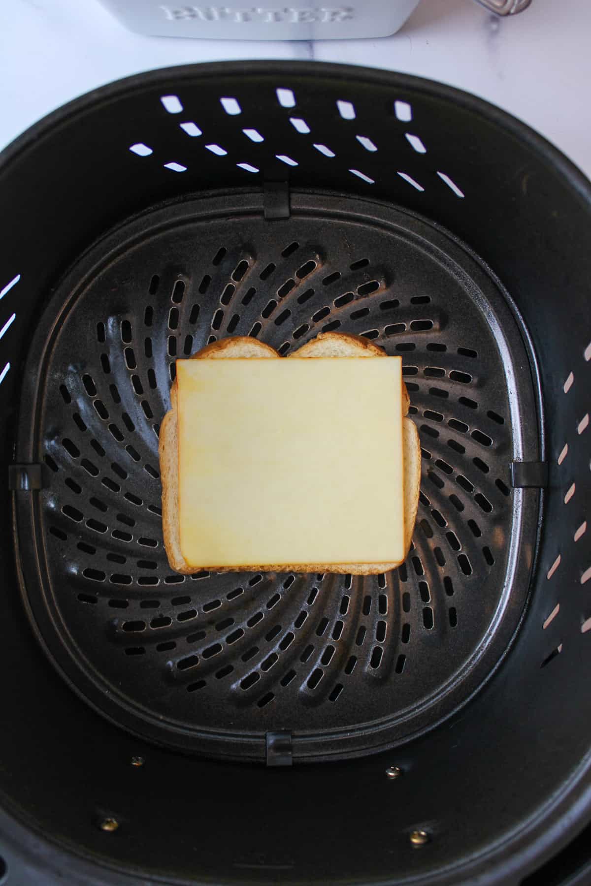 cheese on top of a slice of bread in an air fryer basket.