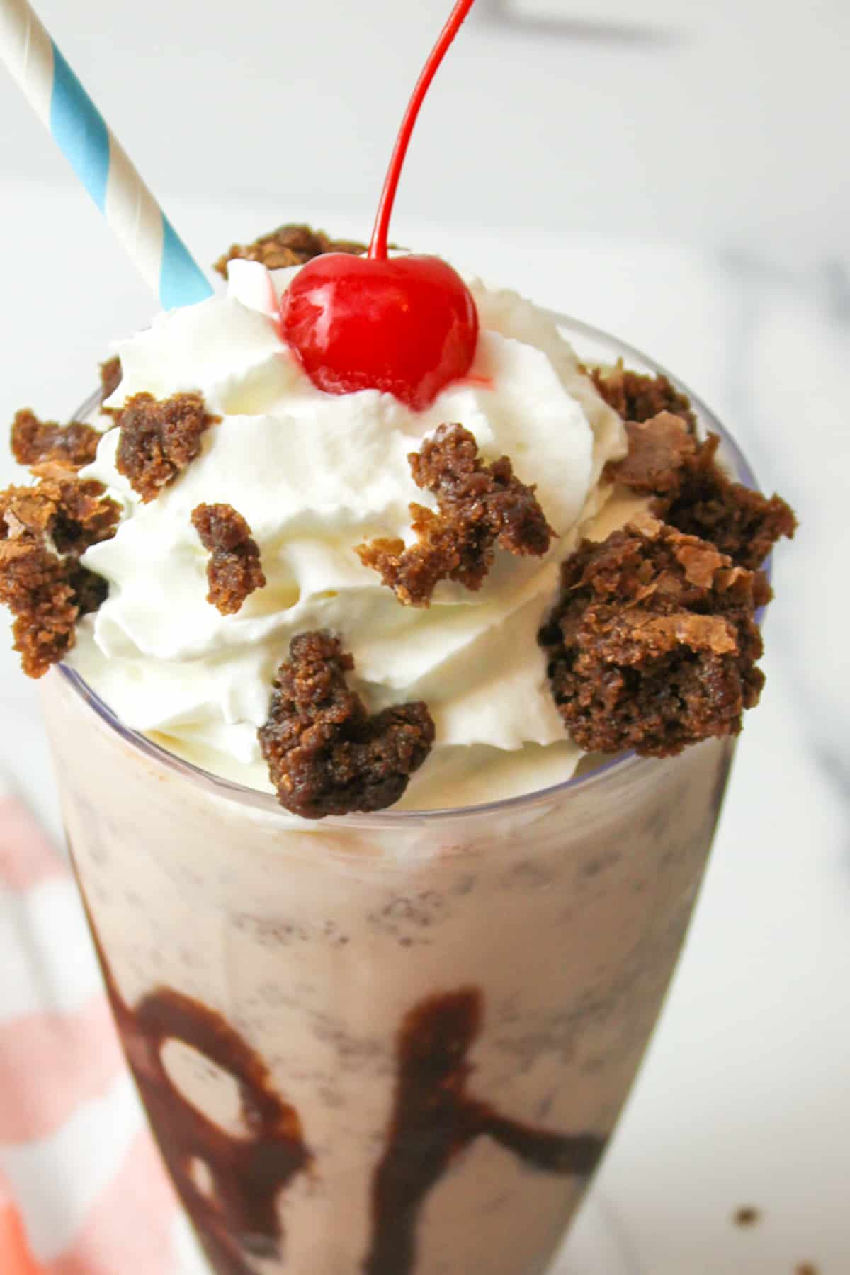 an upclose view of a brownie milkshake garnished with whipped cream, a cherry, and brownie crumbles