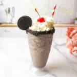 a glass of oreo flavored milkshake made without ice cream and topped with whipped cream, a cherry, and an oreo cookie.