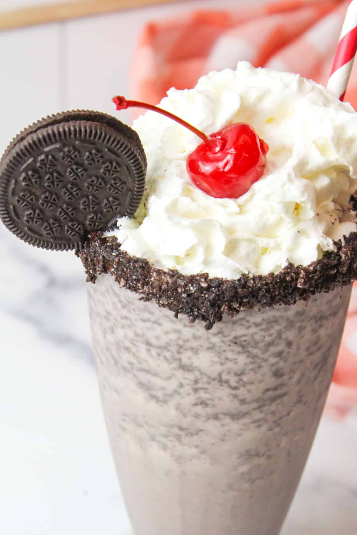 an upclose angled view of a glass of oreo milkshake garnished with whipped cream and a cherry and an oreo cookie