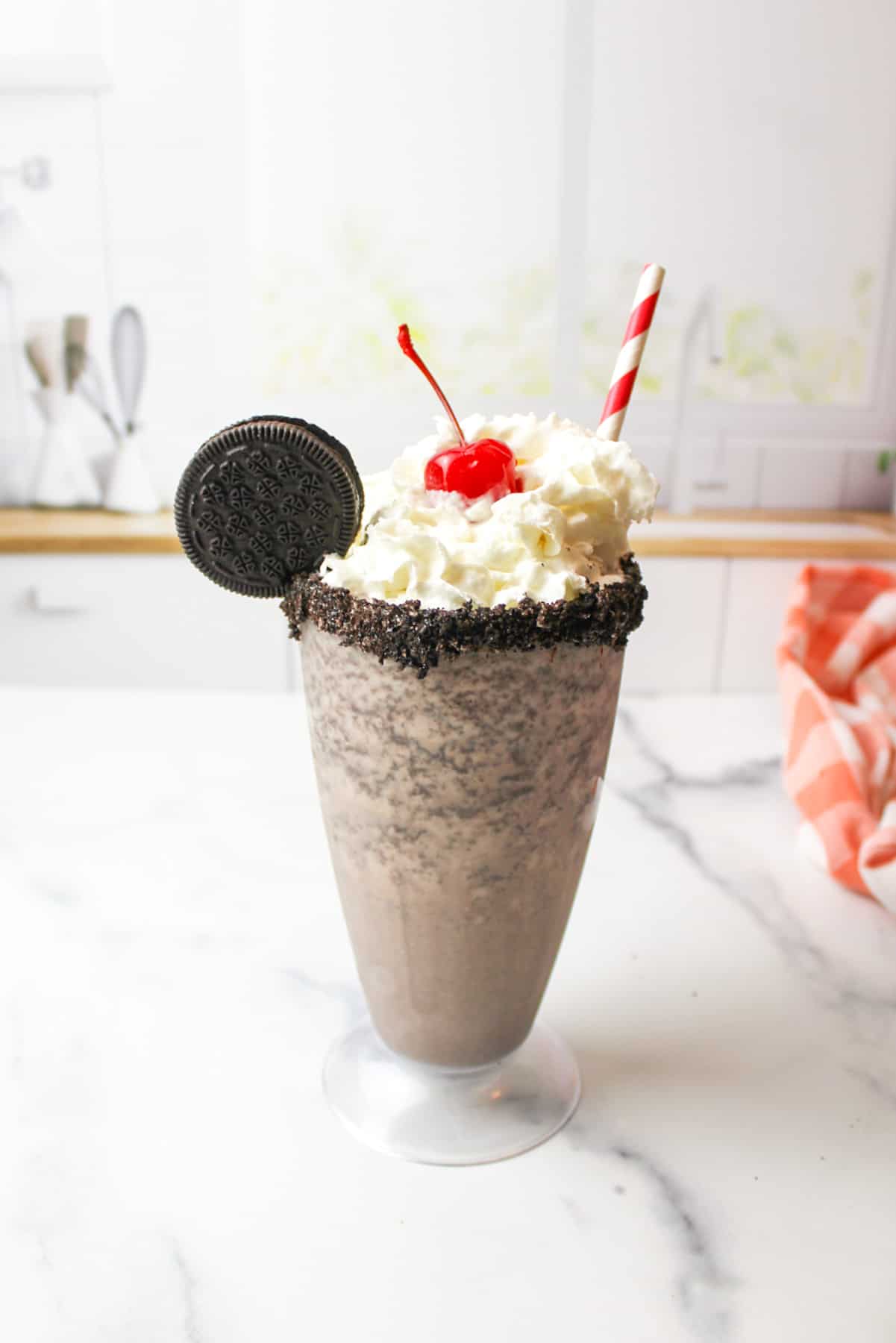 an oreo milkshake in a glass topped with whipped cream and a cherry and garnished with oreo cookies.