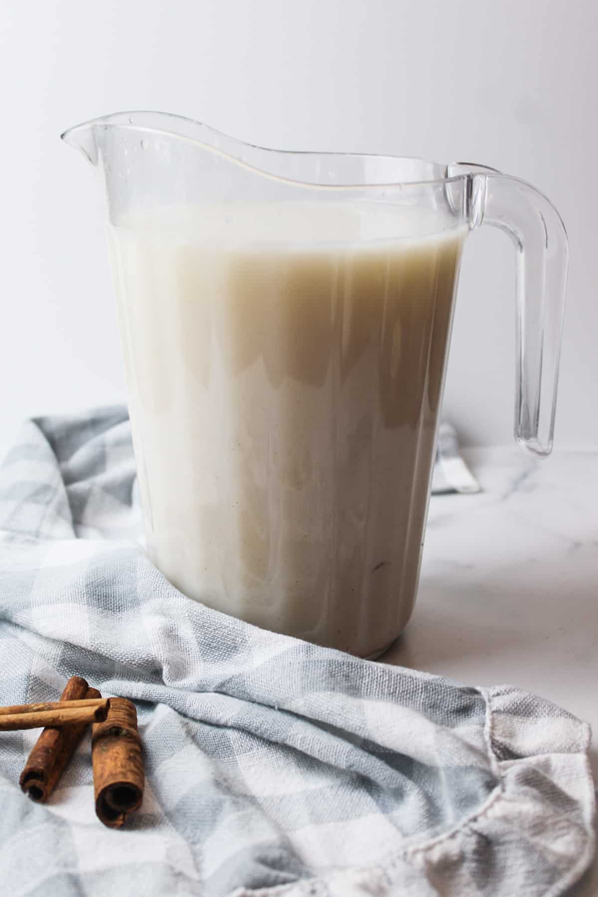 sugar and milk added to cinnamon rice water in a pitcher.