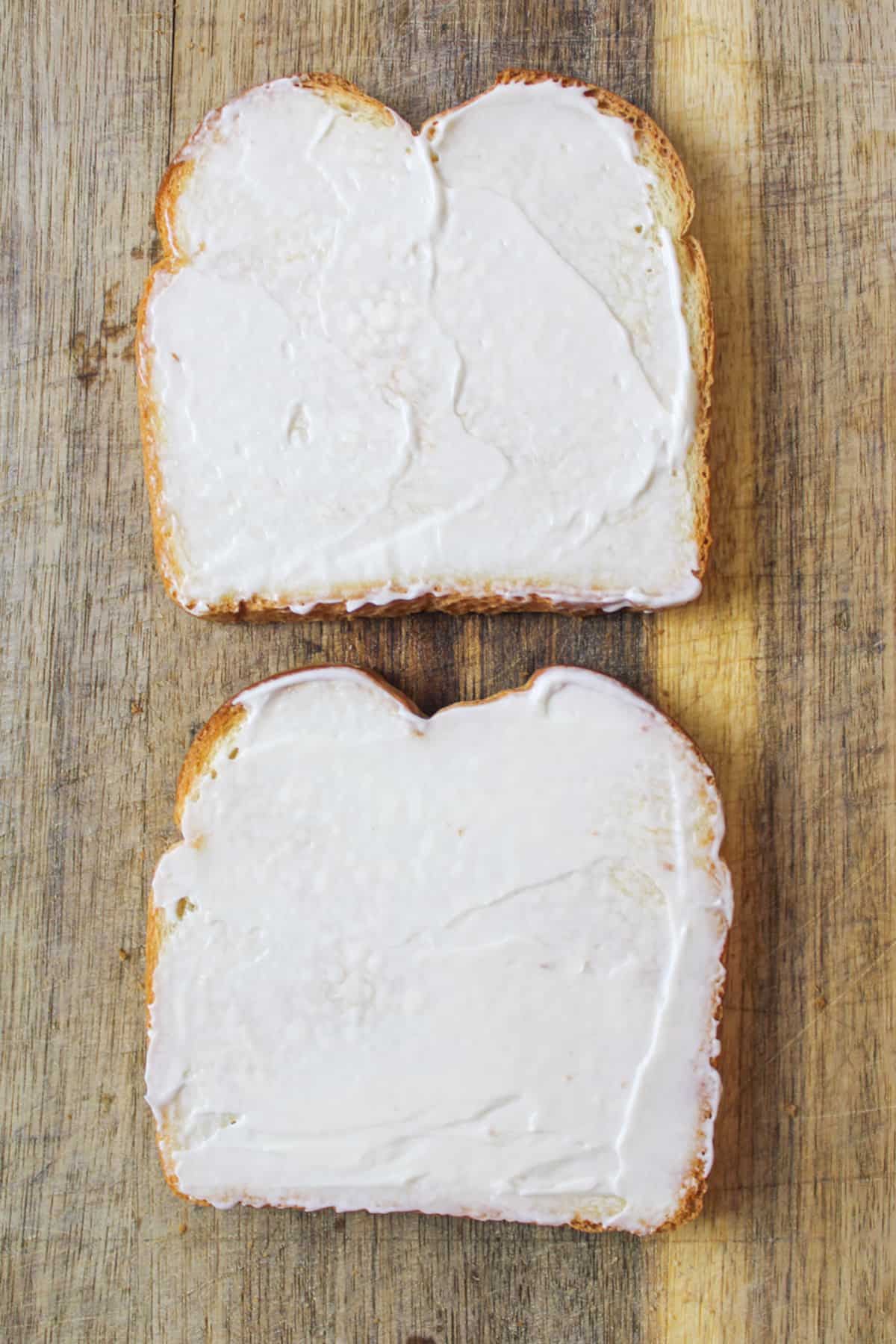 mayo spread on top of two slices of bread on a cutting board.