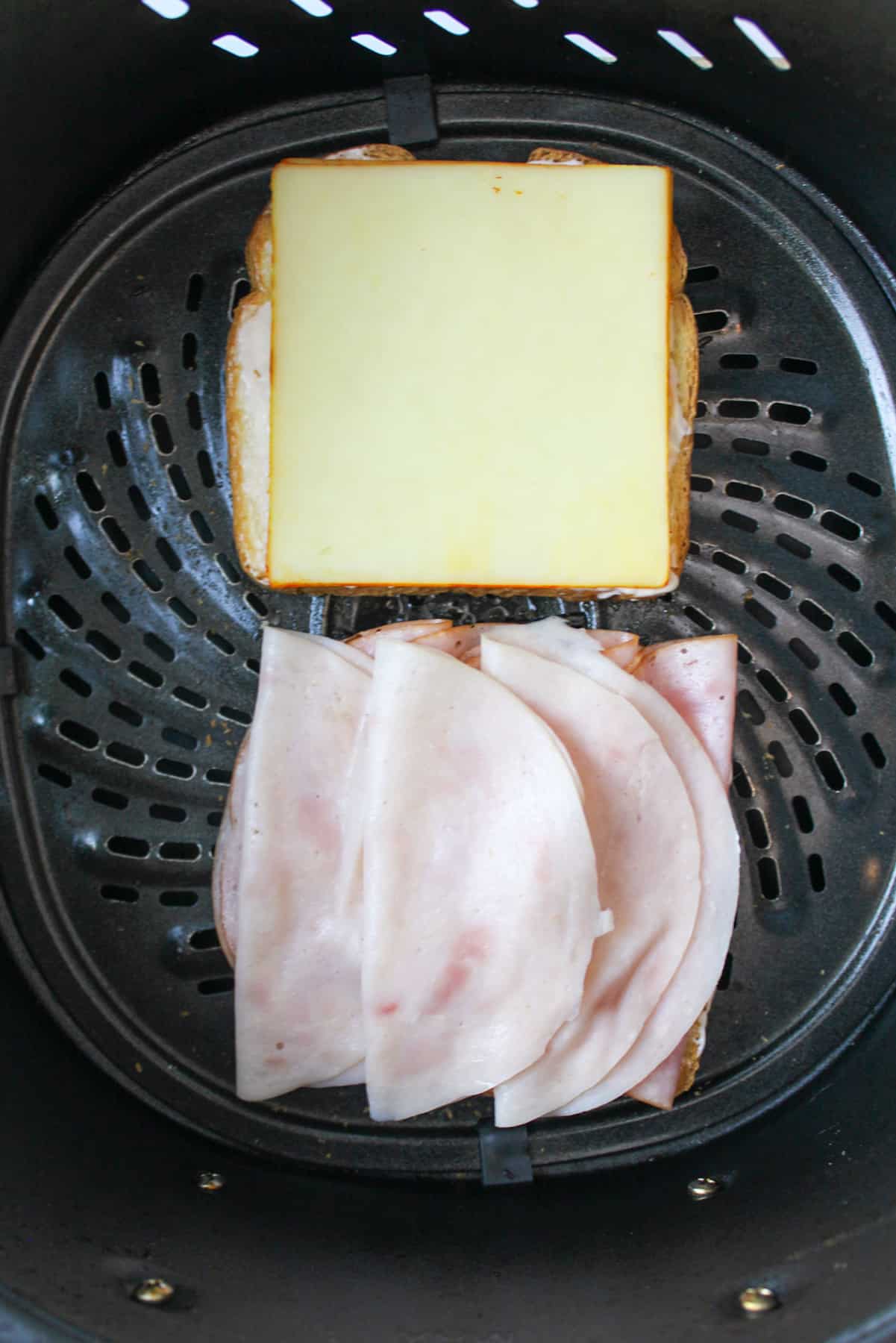 meat and cheese on slices of bread in air fryer basket