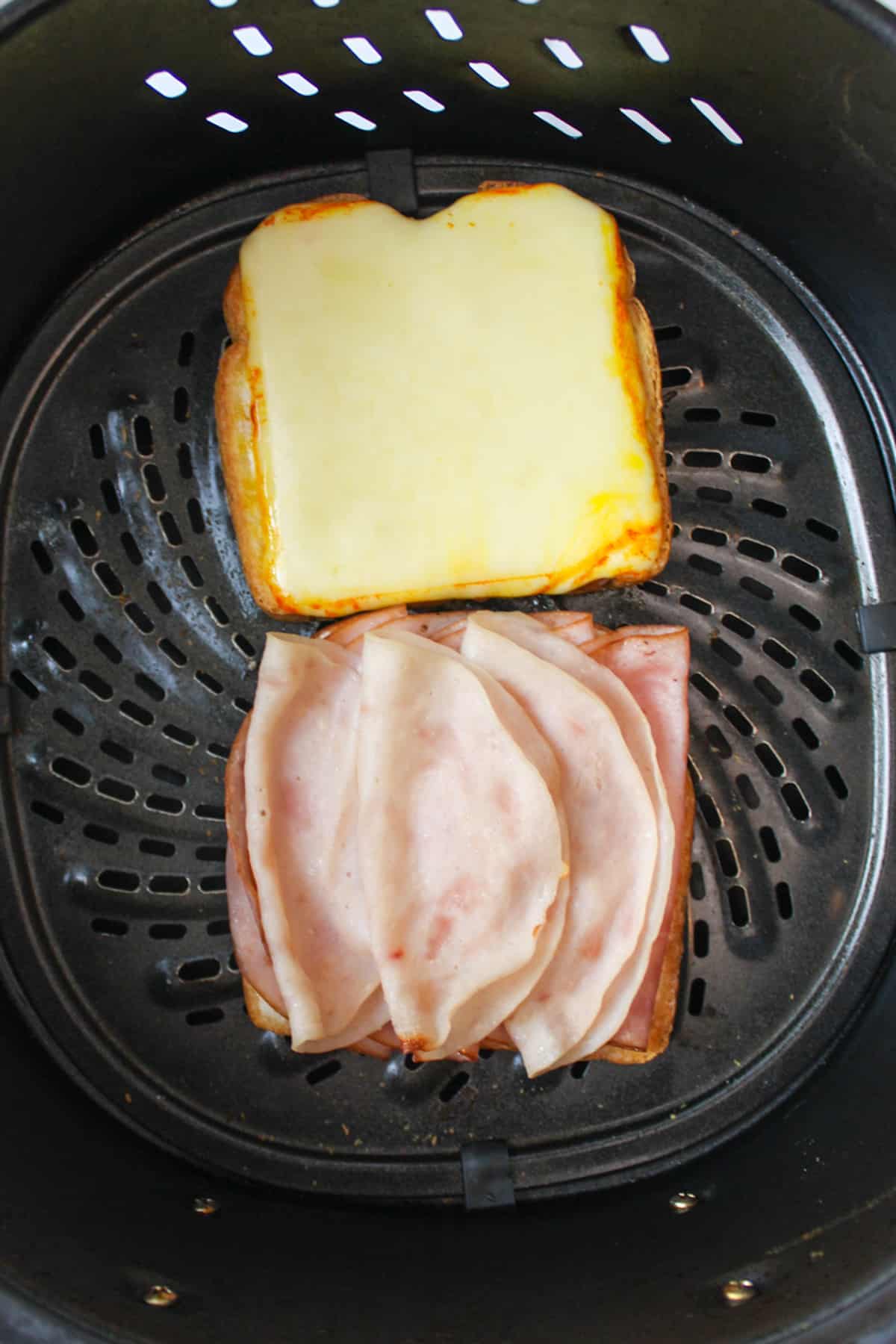 toasted meat and cheese on bread in air fryer basket.