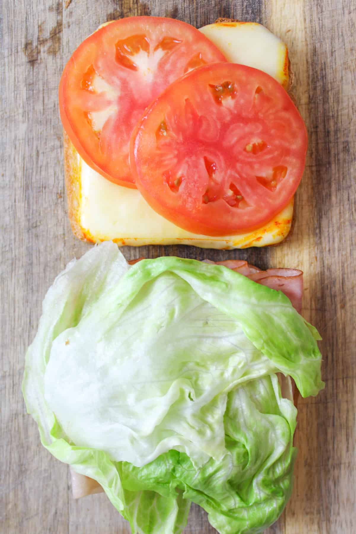 Tomatoes and cheese on one bread slice; meat and lettuce on the other.