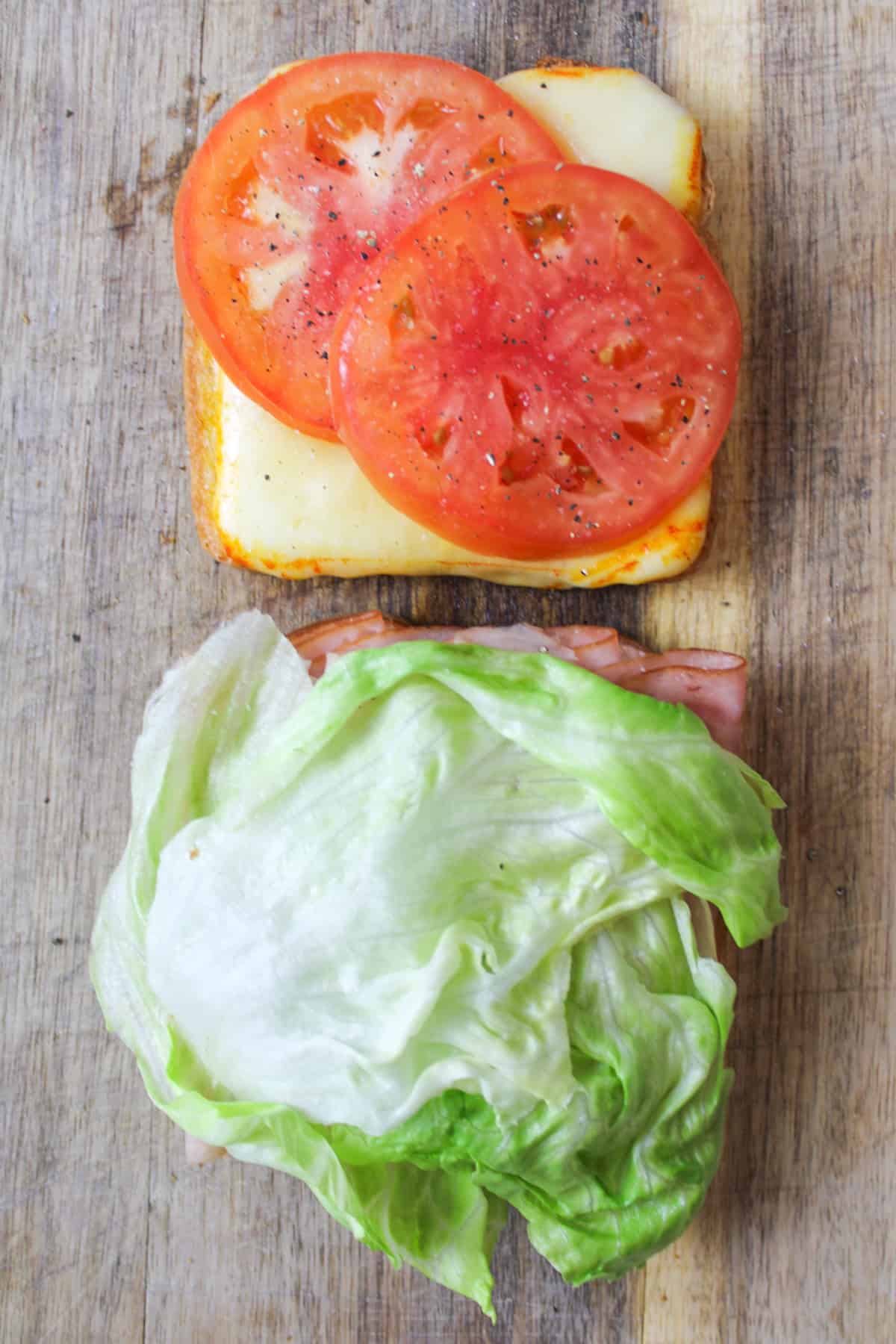 Open-faced club sandwich: tomatoes, cheese, salt, pepper on one; meat, lettuce on the other.