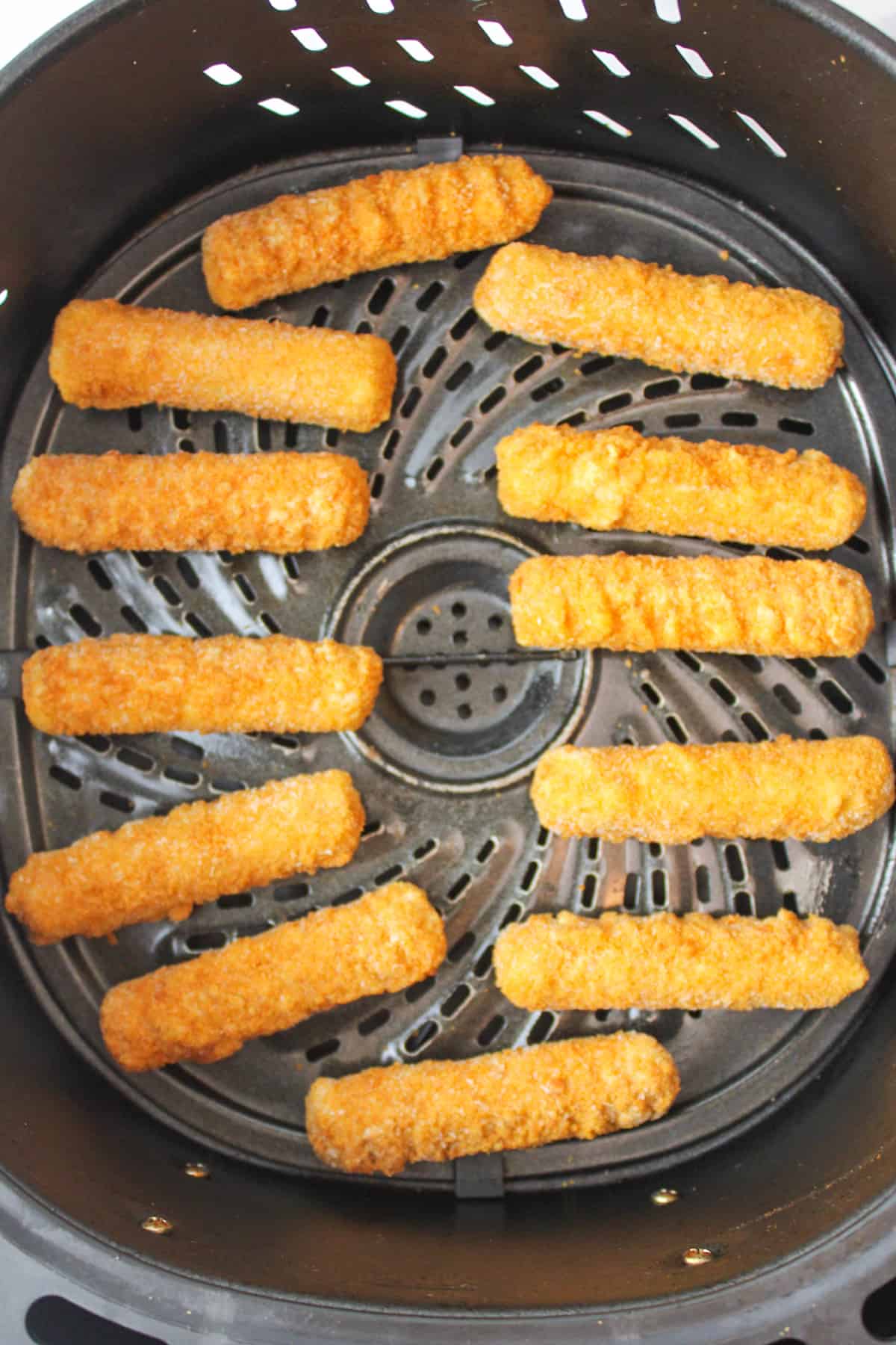 frozen mozzarella sticks in an air fryer basket.