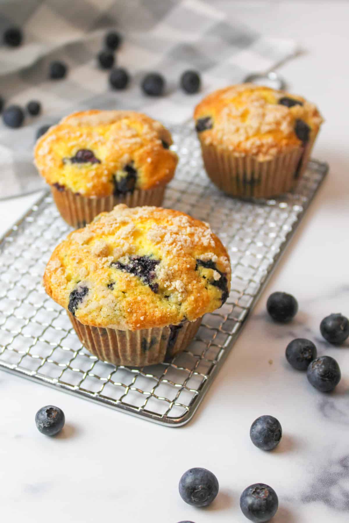 three blueberry muffins made with cake mix resting on a wire rack with fresh blueberries around it