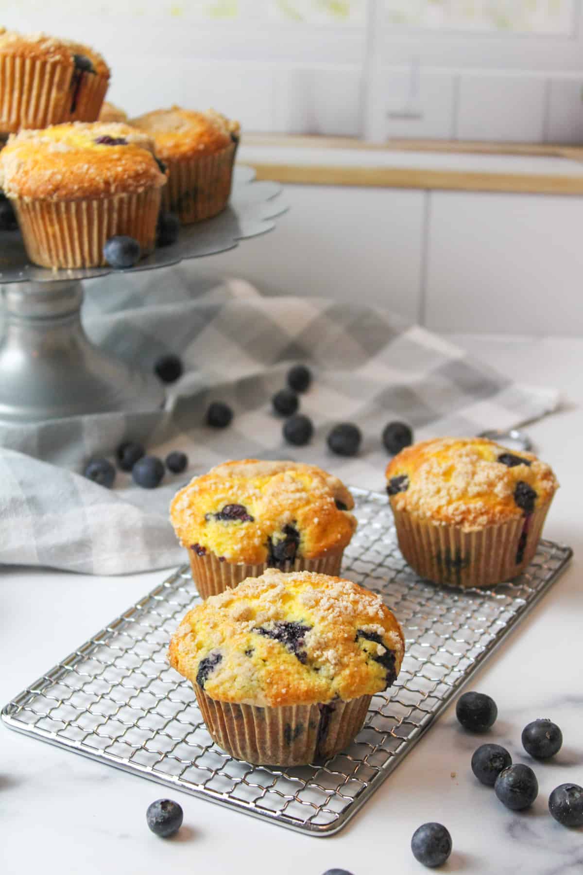 several blueberry muffins on a wire rack and cake stand.