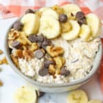a close up of a bowl of chunky monkey flavored overnight oats topped with walnuts chocolate chips and banana slices