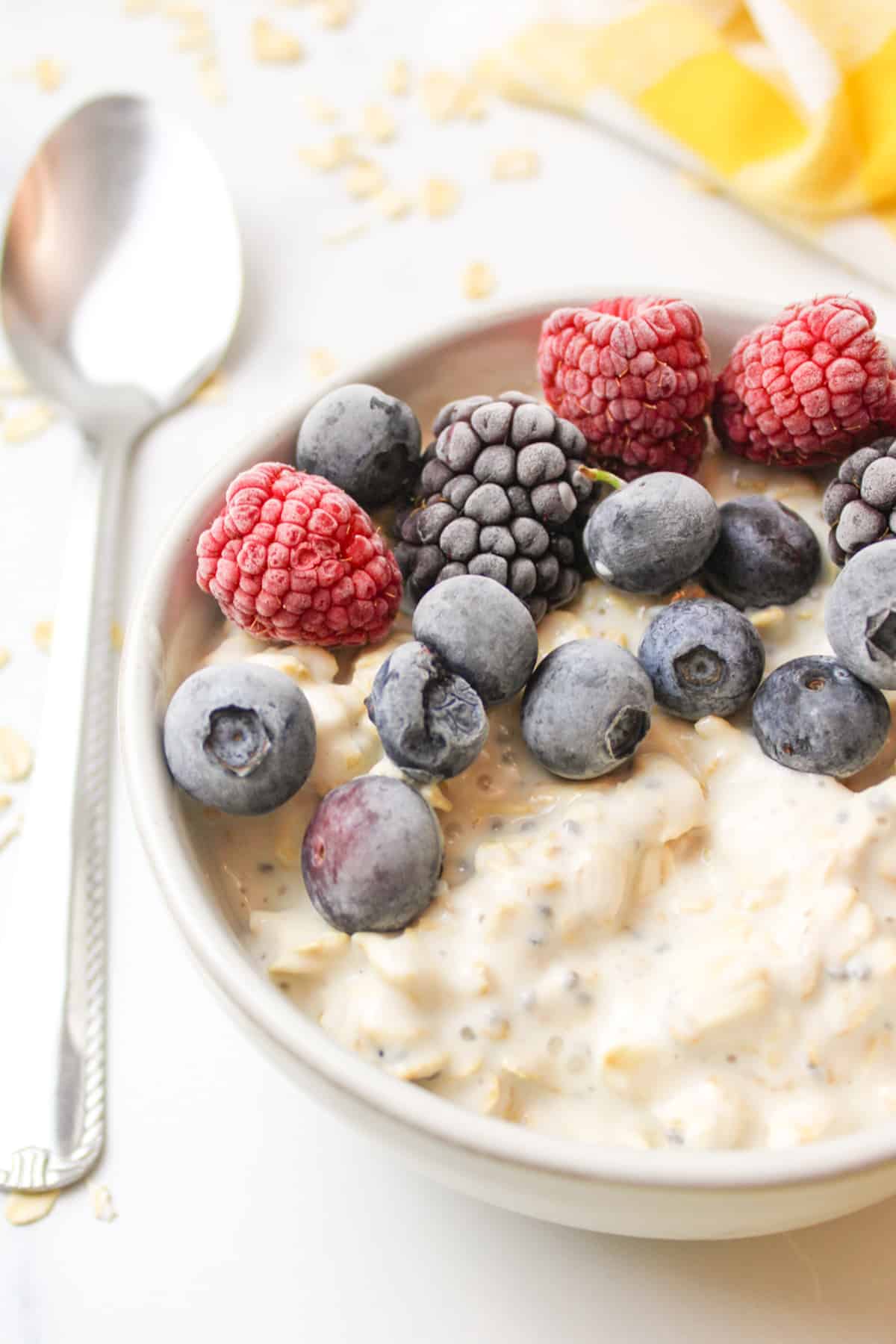 a bowl of overnight oats topped with frozen berries next to a spoon.