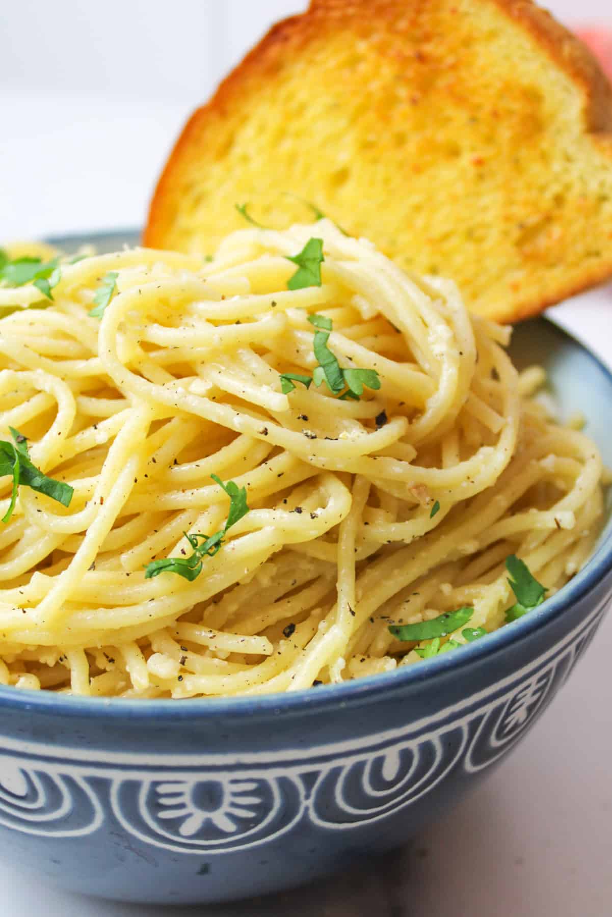 an upclose view of lemon garlic butter pasta in a blue bowl with a piece of garlic toast.