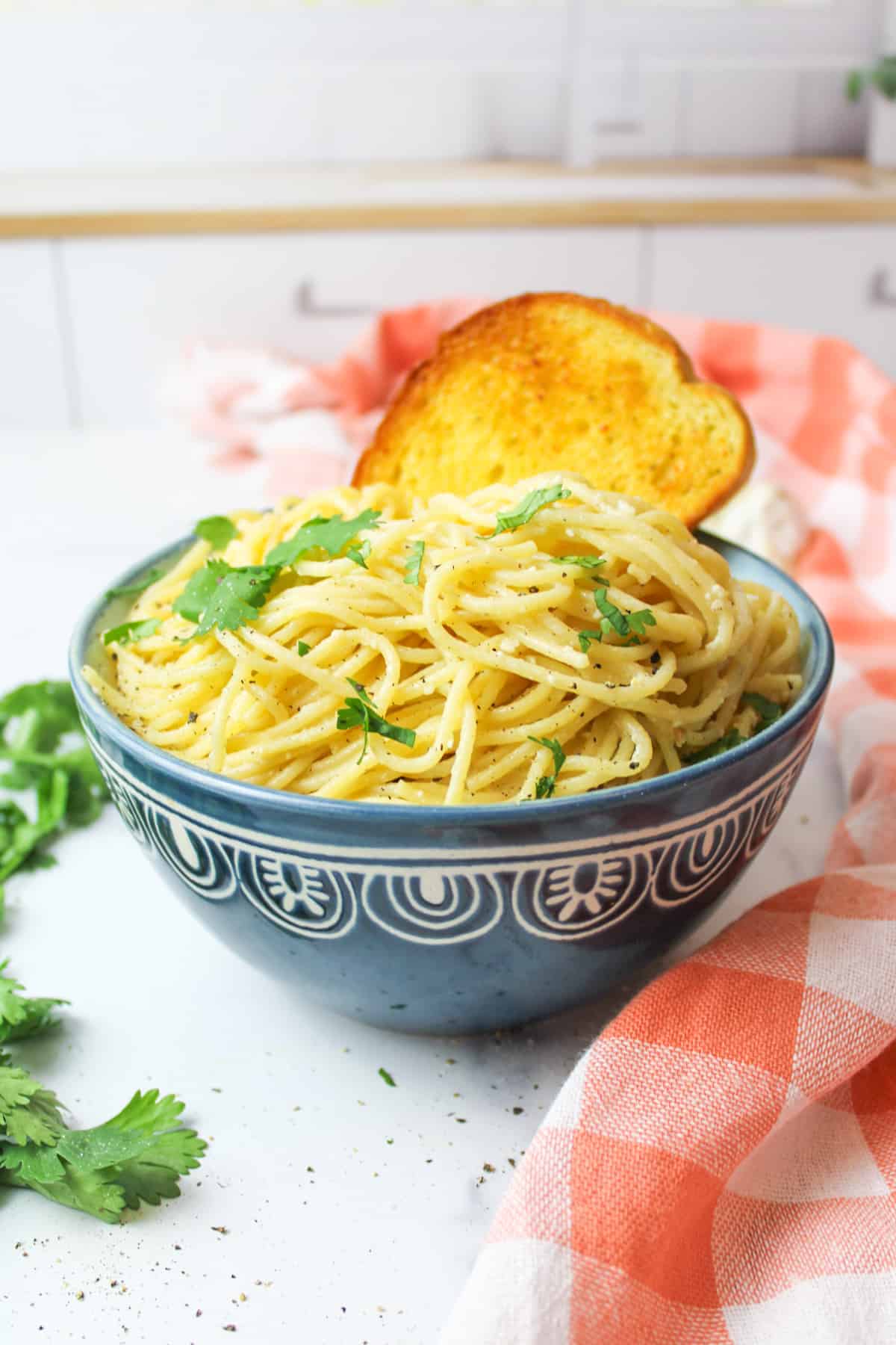 a blue bowl filled with lemon garlic pasta and a piece of garlic bread