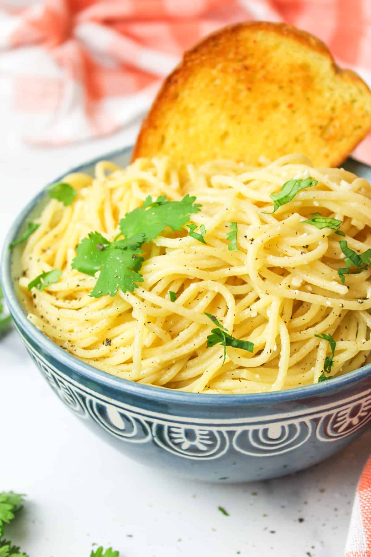 Blue bowl with lemon garlic butter pasta, garnished with green parsley leaves.