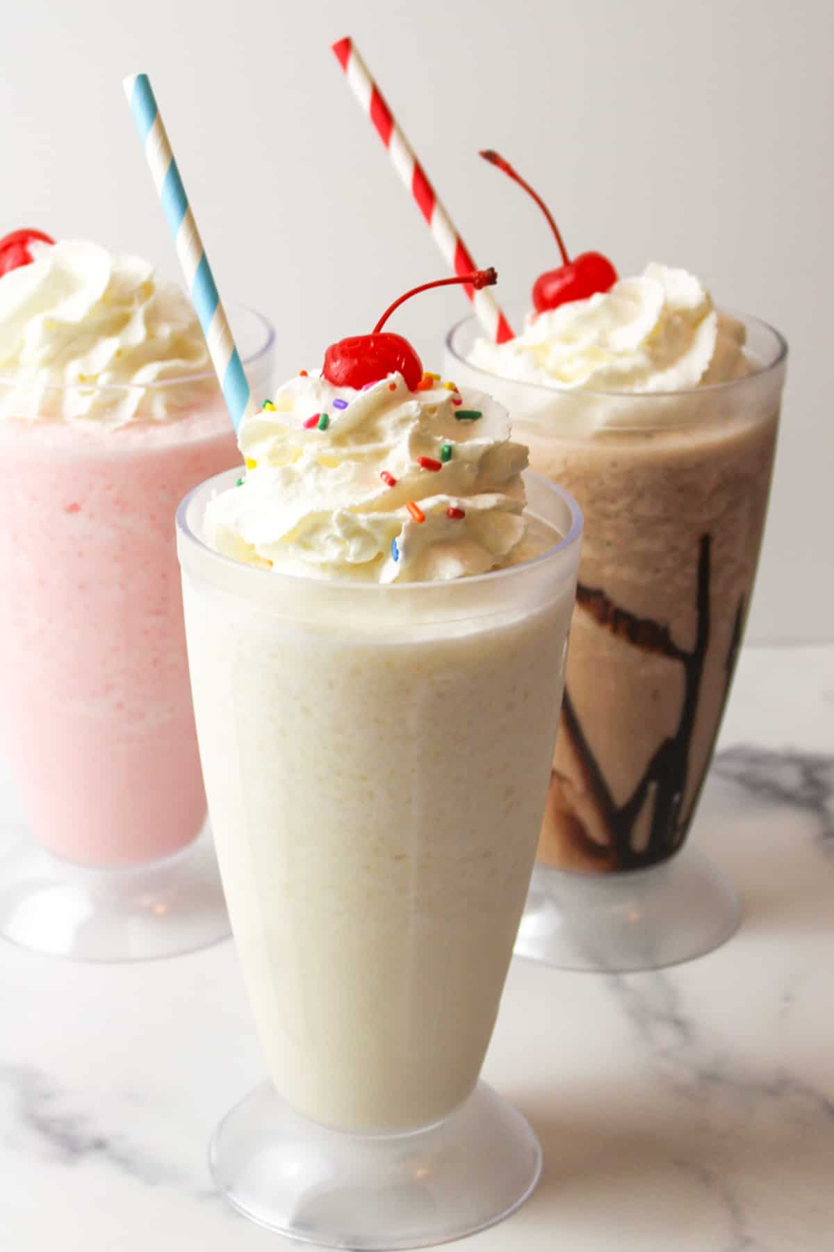 three milkshakes made without ice cream and topped with whipped cream and cherries and given a striped straw.
