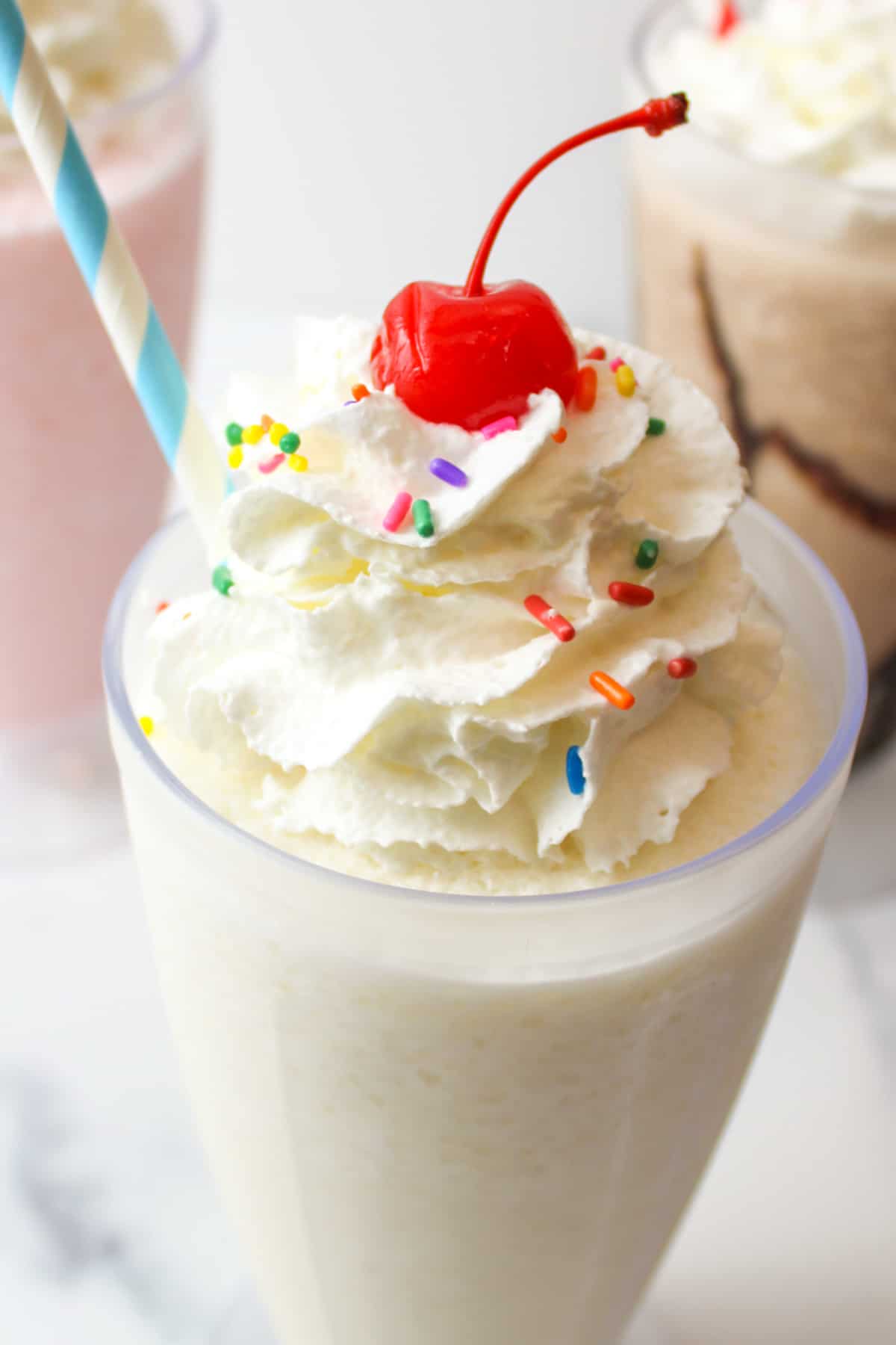 vanilla milkshake topped with whipped cream sprinkles and a cherry