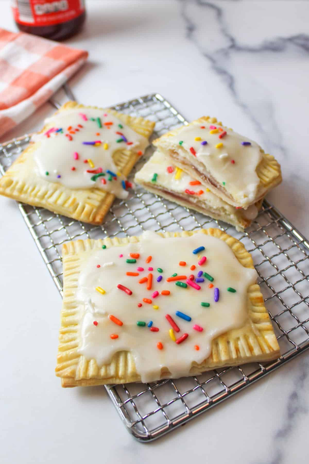 three Homemade Strawberry Pop Tarts on a wire rack with one broken in half to revel the filling.