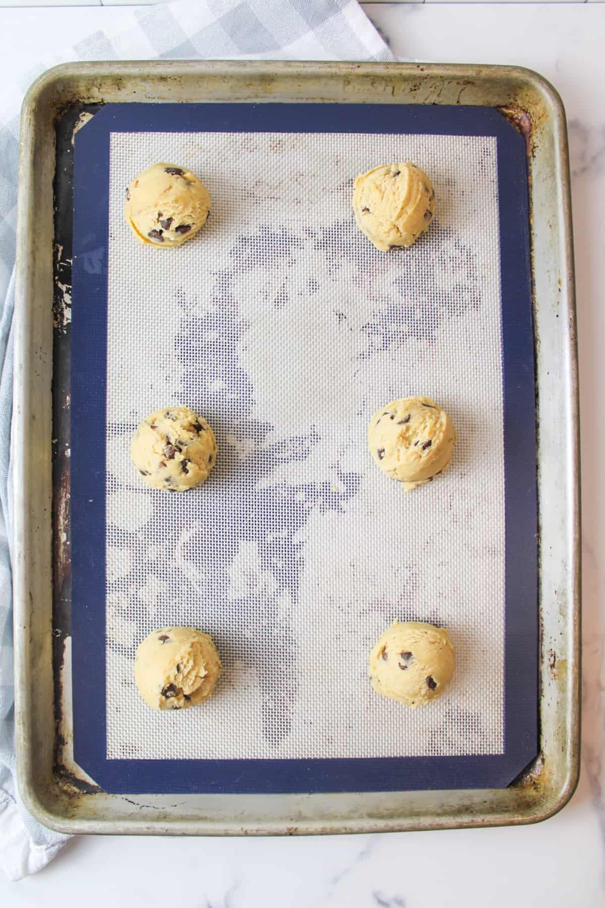 scooped cookie dough on a silicone mat lined baking sheet
