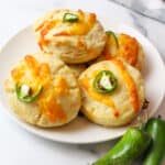 several jalalpeno cheddar biscuits on a white plate next to fresh jalapenos