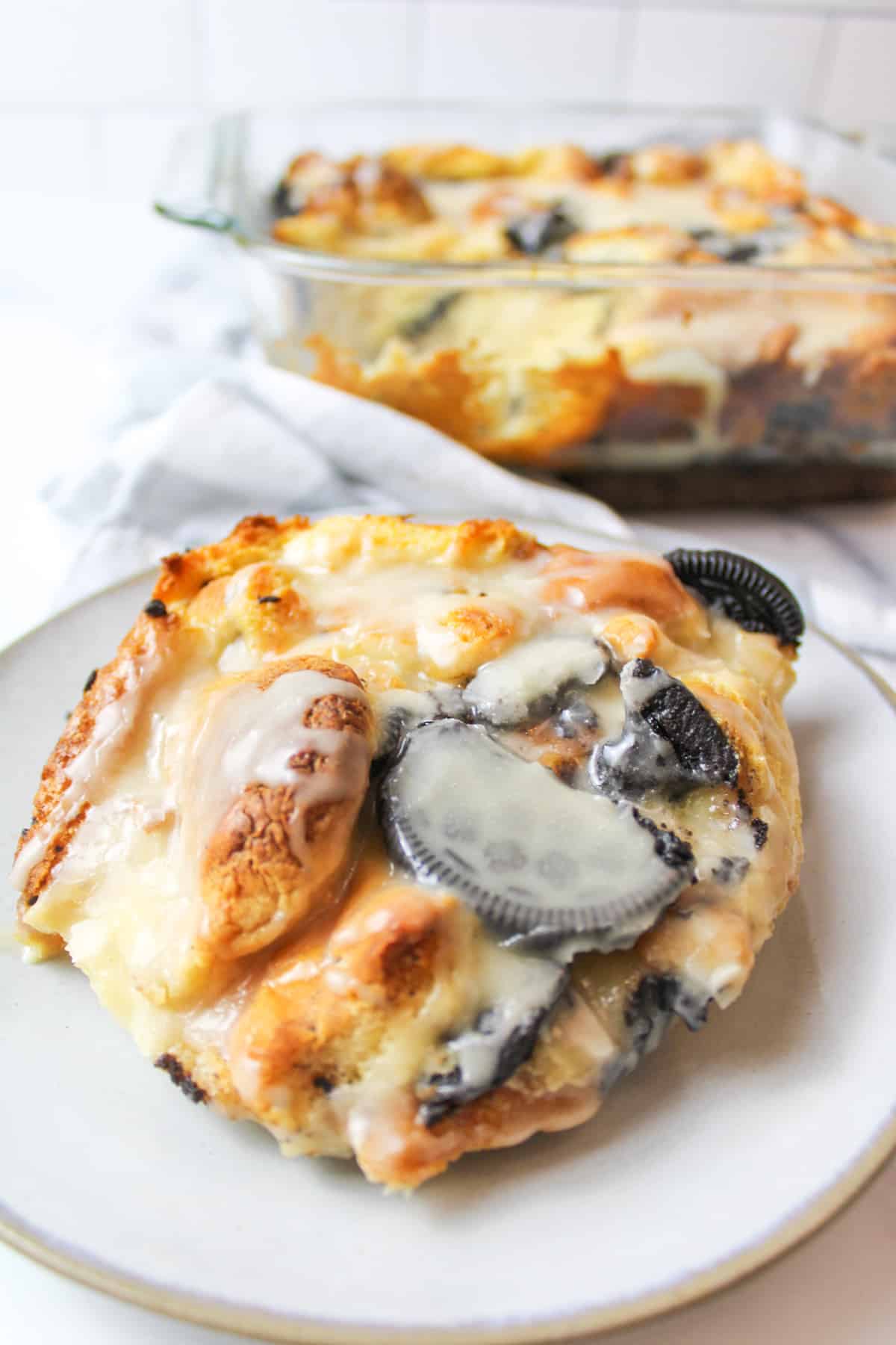 serving of oreo bread pudding on a plate with more in a glass baking dish in background