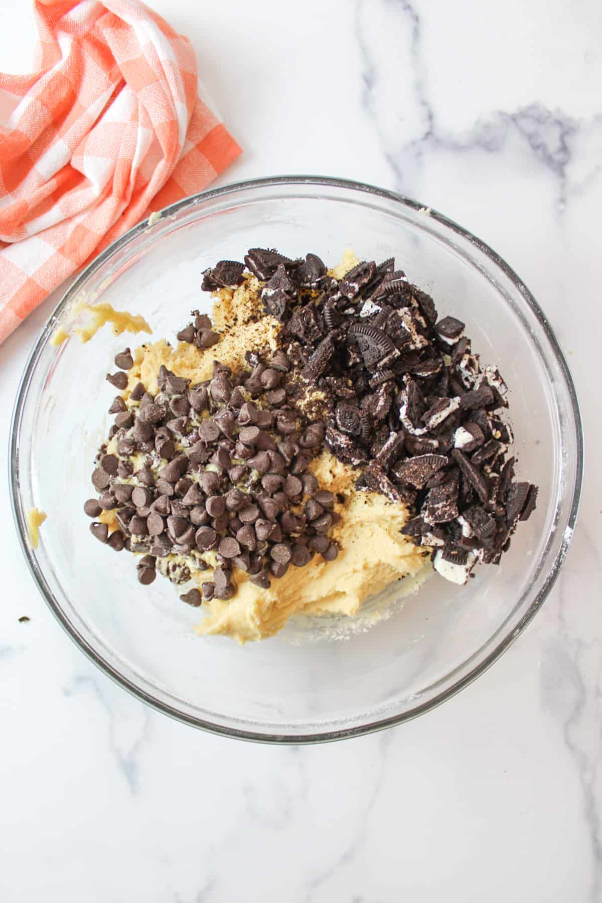 cookie dough in a mixing bowl with crumbled oreo cookies and chocolate chips