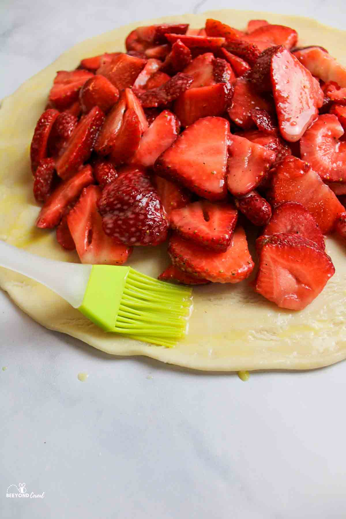 strawberry filling on pie crust with a pastry brush moistening the crust edges.