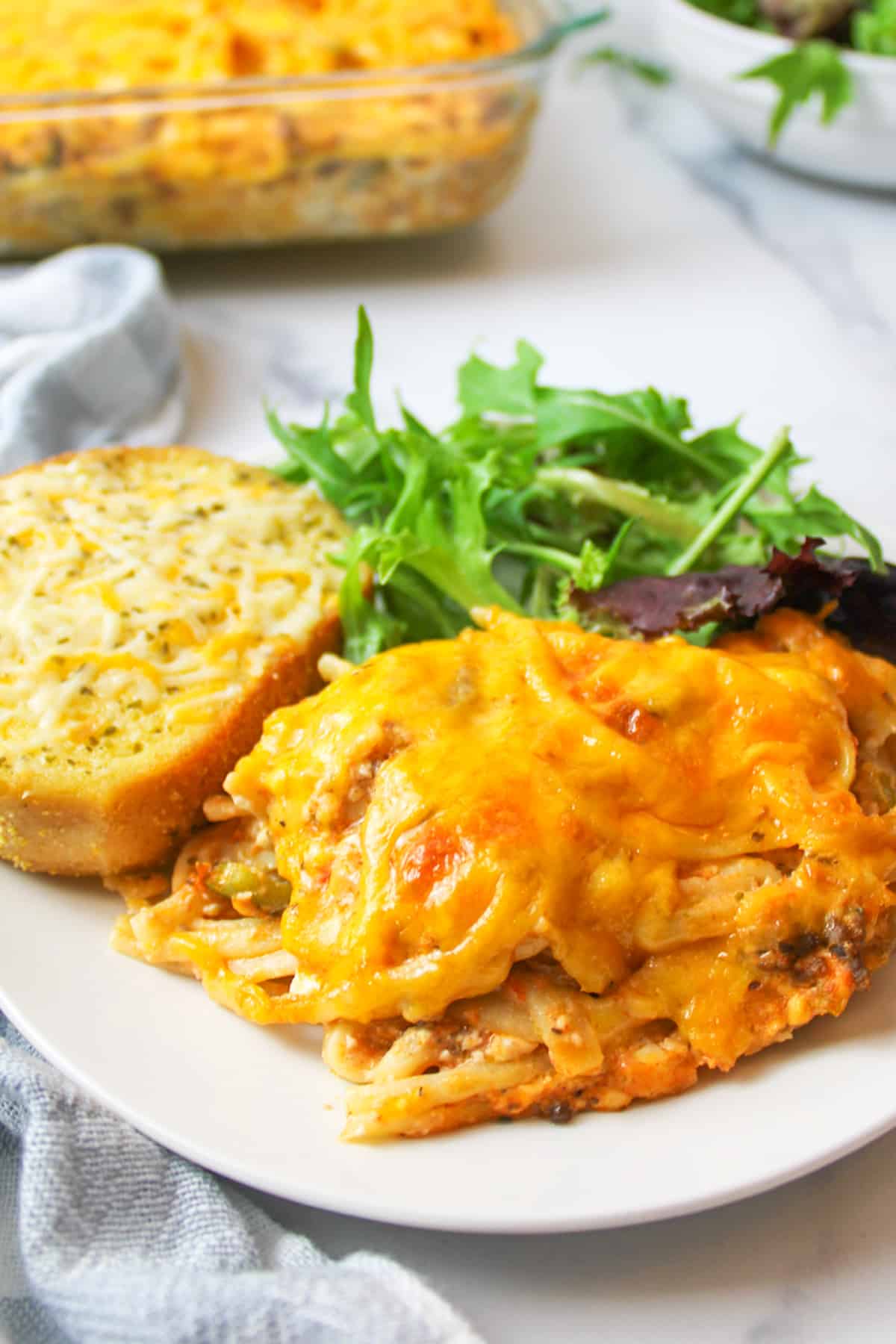 Southern spaghetti bake on a plate with garlic bread and salad.