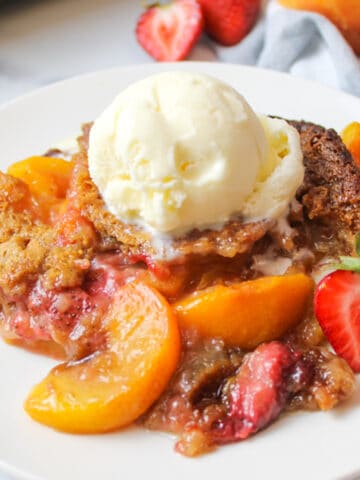 a serving of strawberry peach cobbler on a plate with a scoop of vanilla ice cream on top.