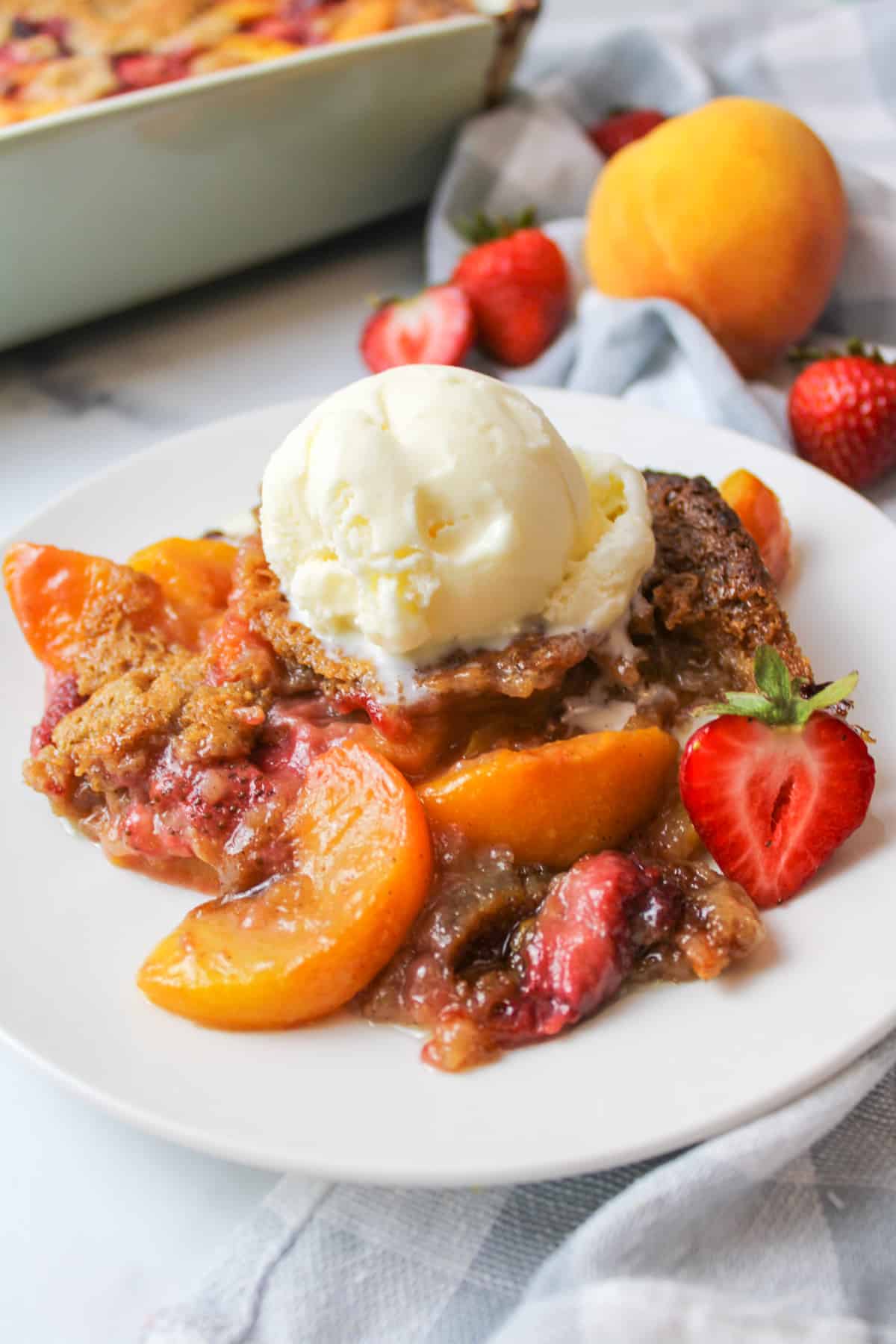 a serving of strawberry peach cobbler on a plate topped with ice cream.