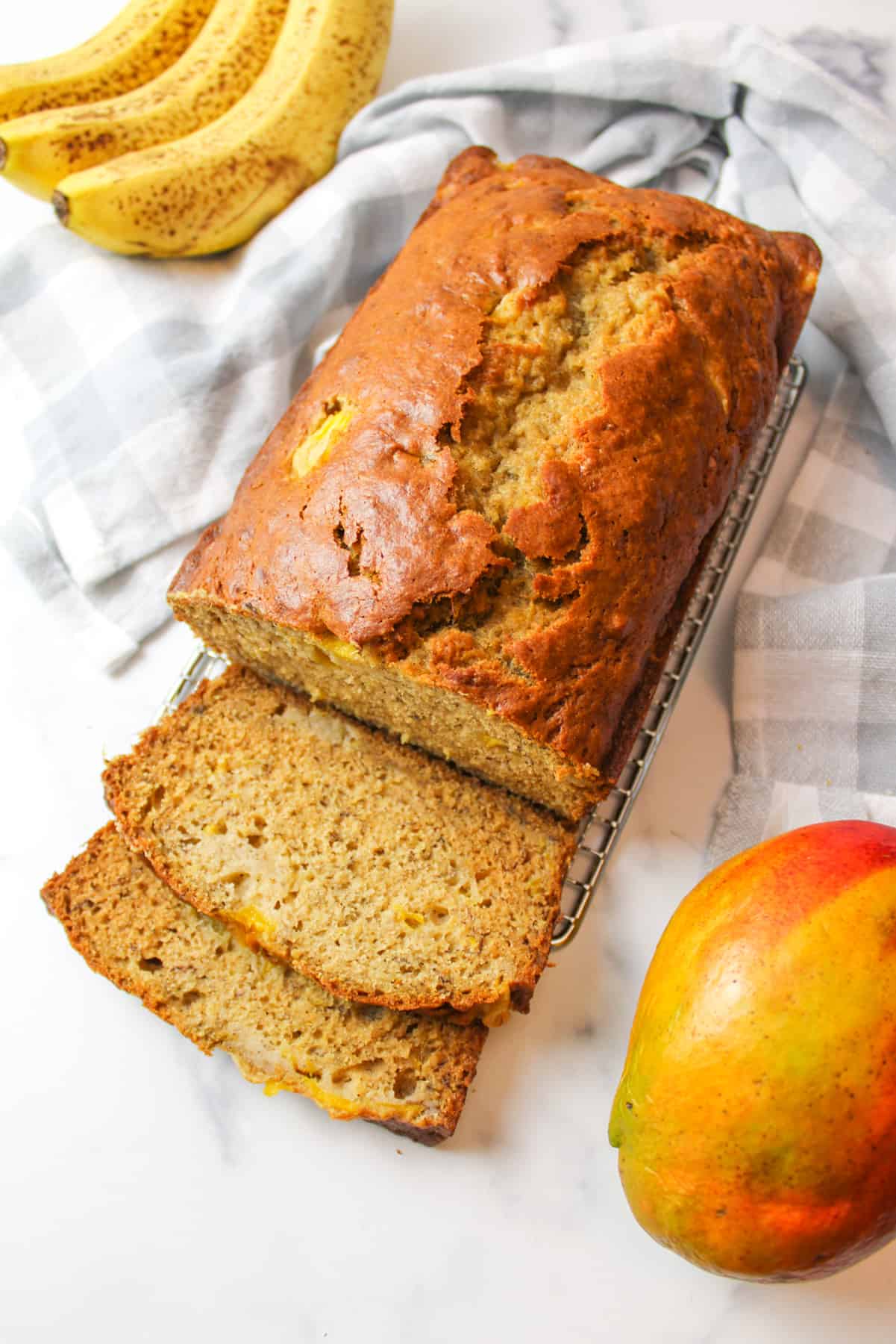 sliced mango banana bread on a wire rack next to ripe bananas and a mango