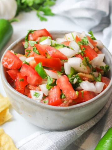 a bowl of fresh tomato jalapeno salsa with chips and jalapenos to the sides