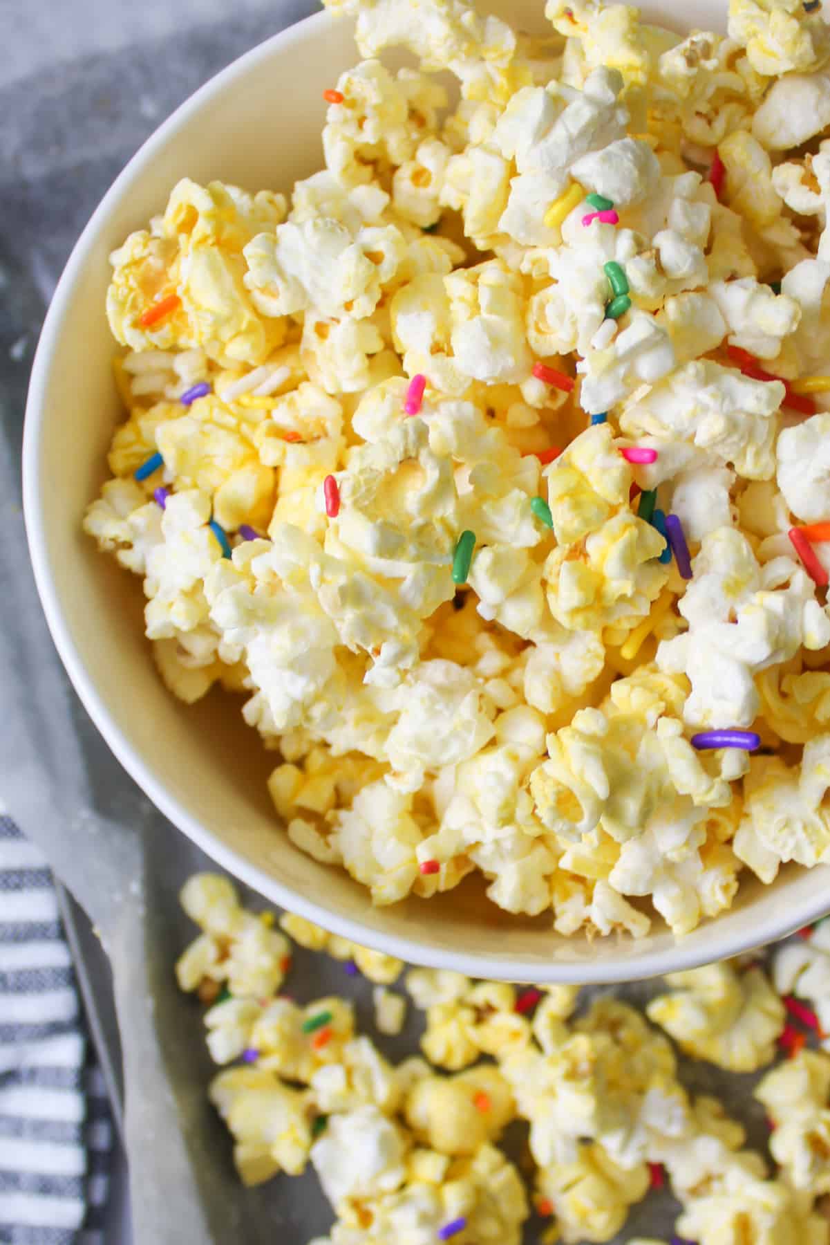 almond bark popcorn with sprinkles in a bowl and some on baking sheet below it.