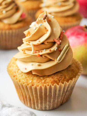 apple cider cupcakes with caramel frosting and seasonal sprinkles. Fresh apples in background