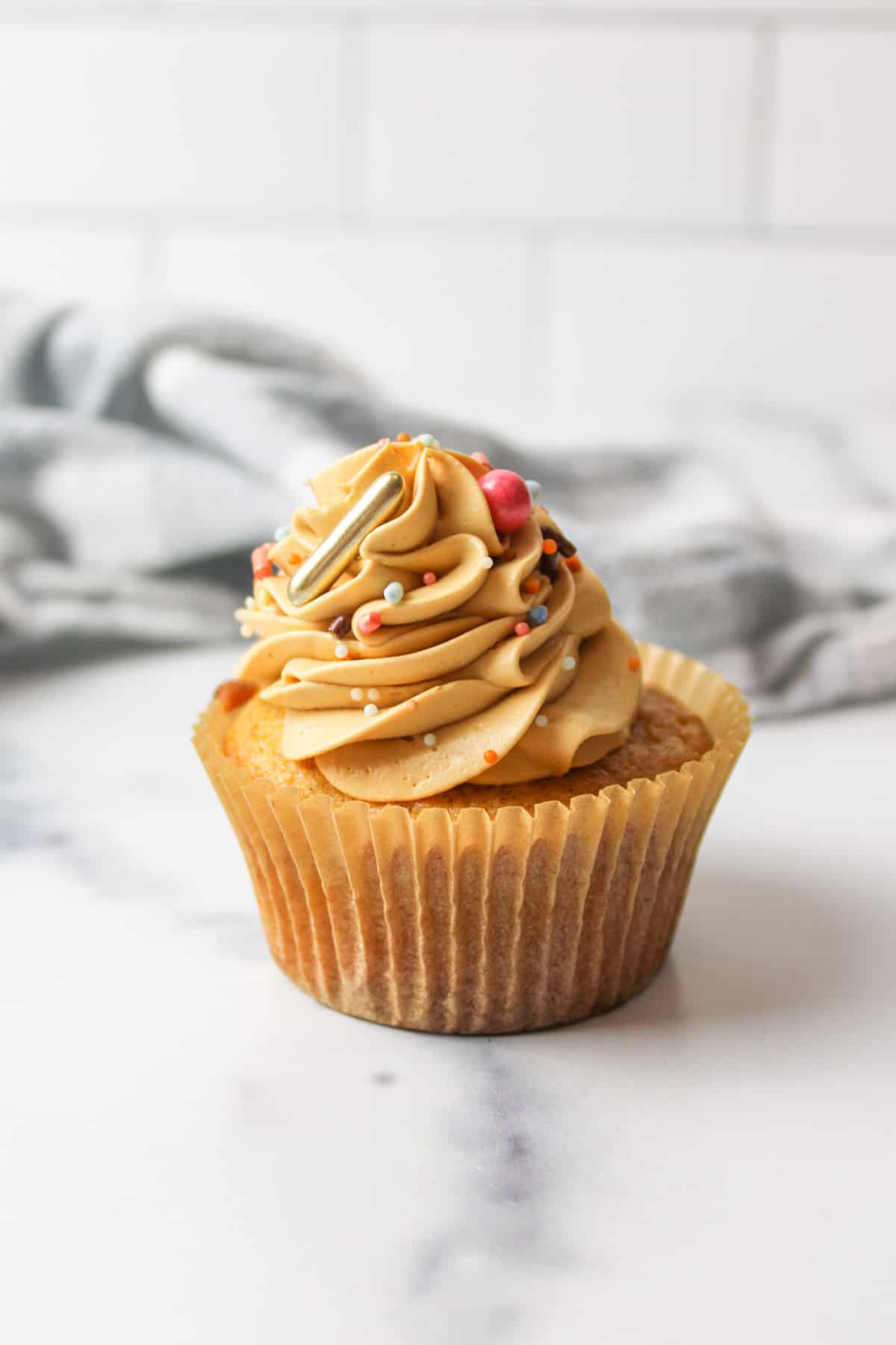 apple cider cupcake with caramel frosting and sprinkles on top.